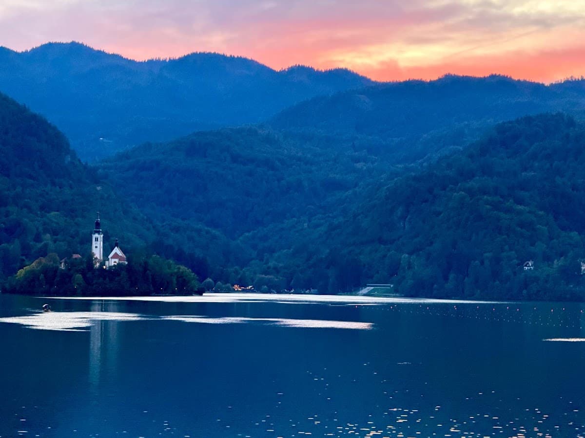 Lake Bled island church at sunset with forested mountains in the background