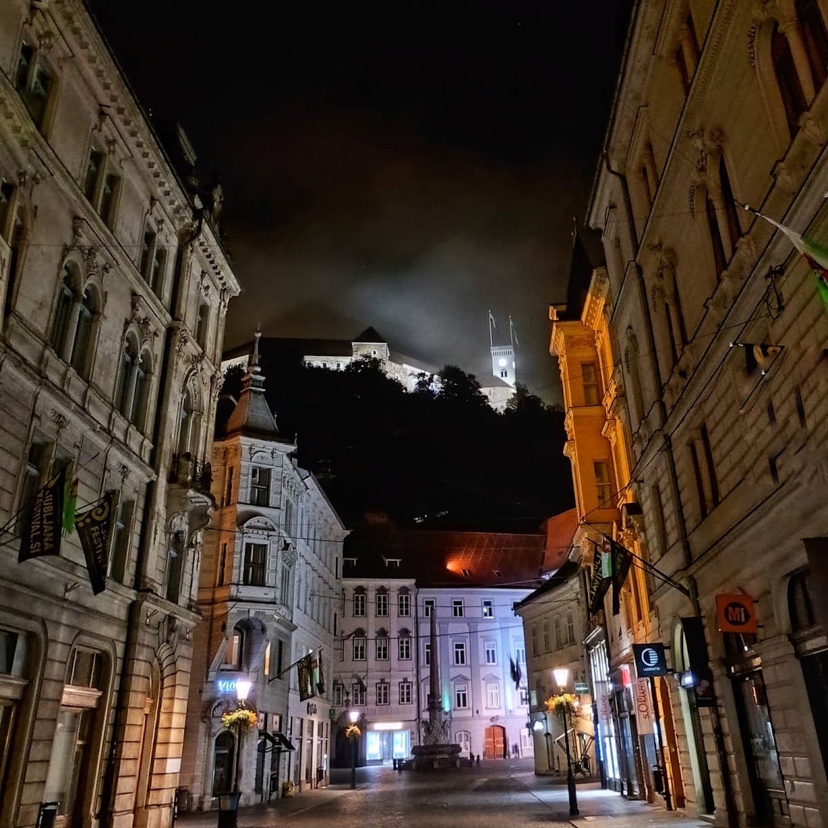 Illuminated historic European street at night with castle on hill in background