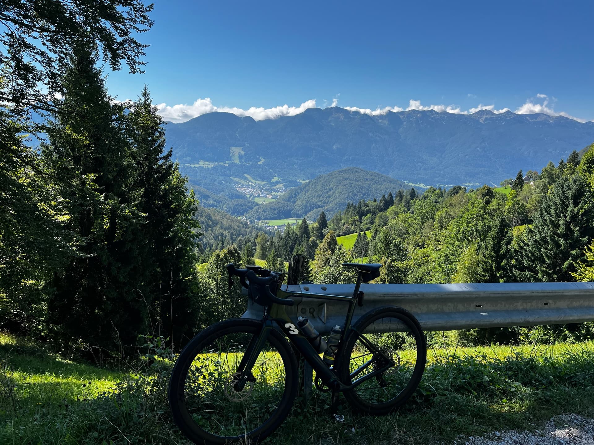 Road bike parked by a guardrail overlooking a lush green alpine valley and mountain range