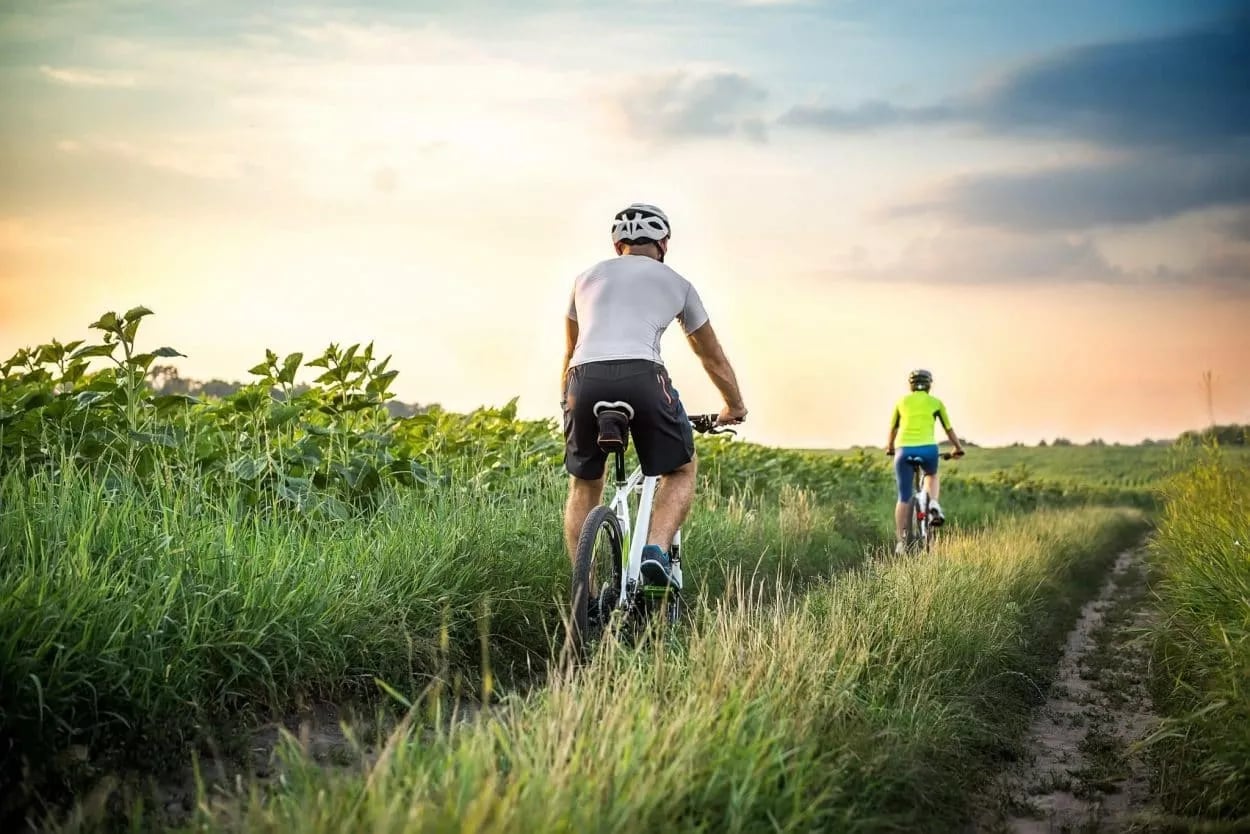 Mountain biking on a dirt path through tall grass and fields at sunset