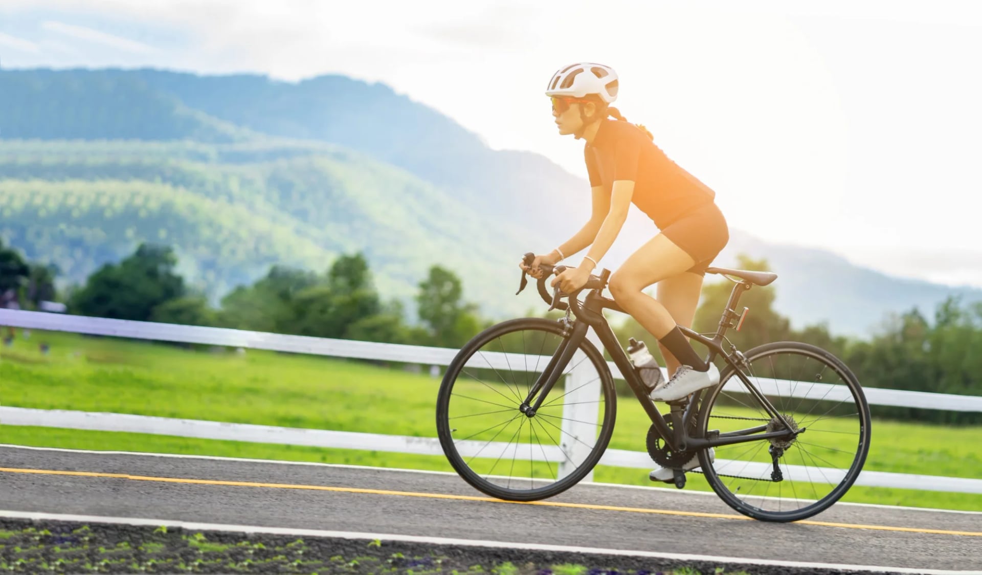 Woman cycling road bike on paved road with green hills and mountains in background