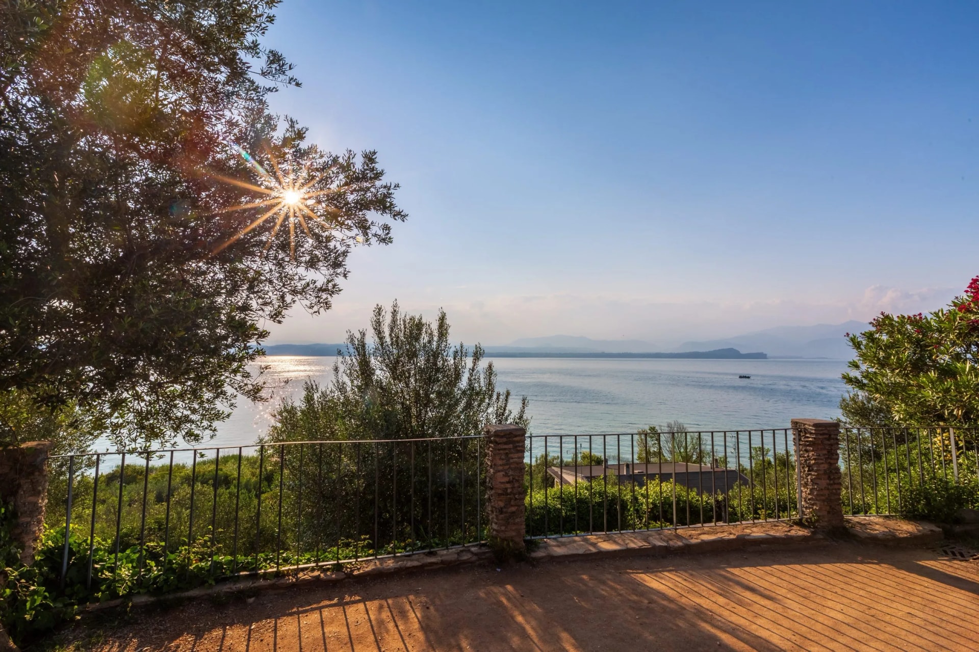 Lake view from terrace with sun flare through olive tree and distant mountains, Sirmione