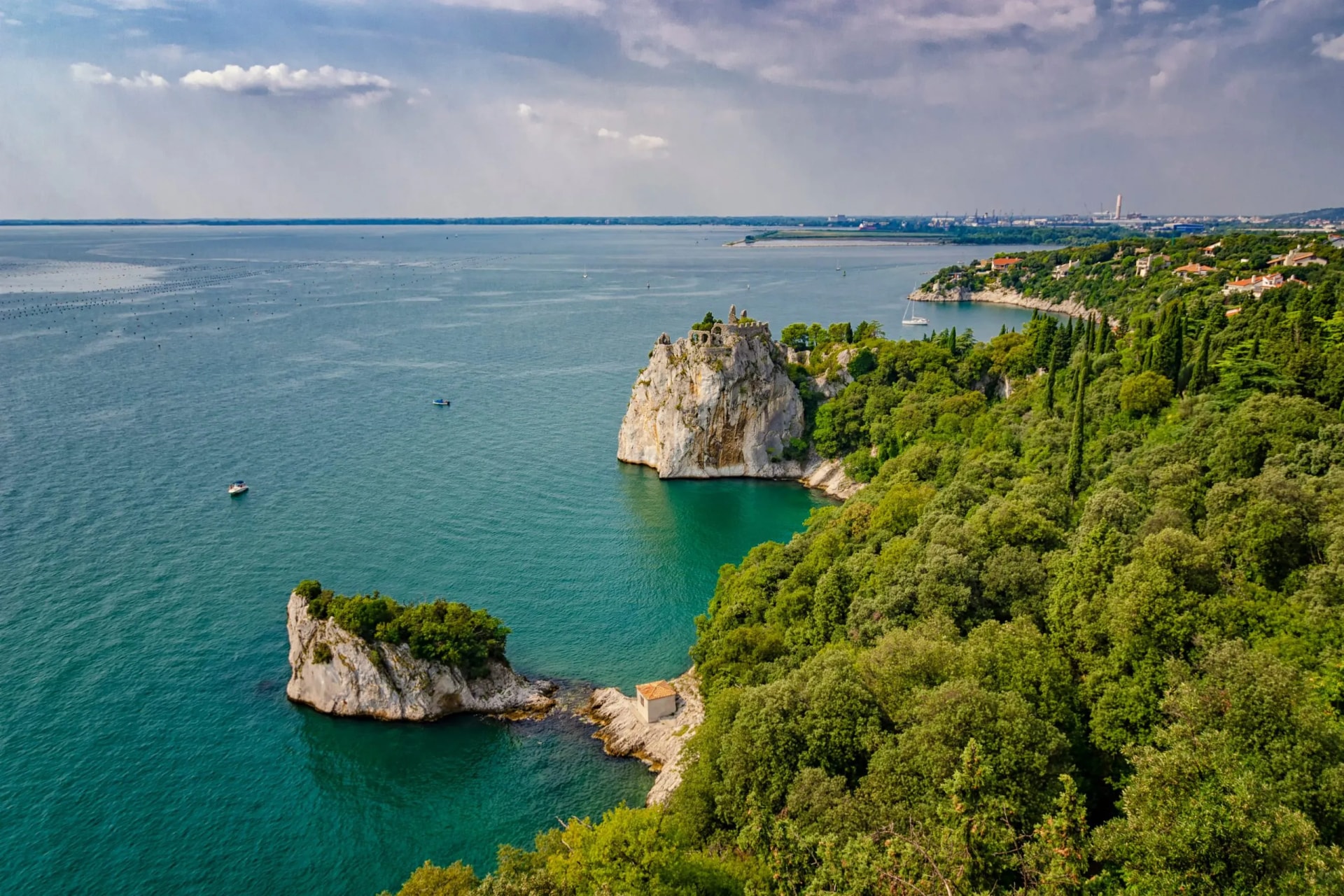 Rocky outcrop with castle ruins above turquoise water of the Gulf of Trieste.