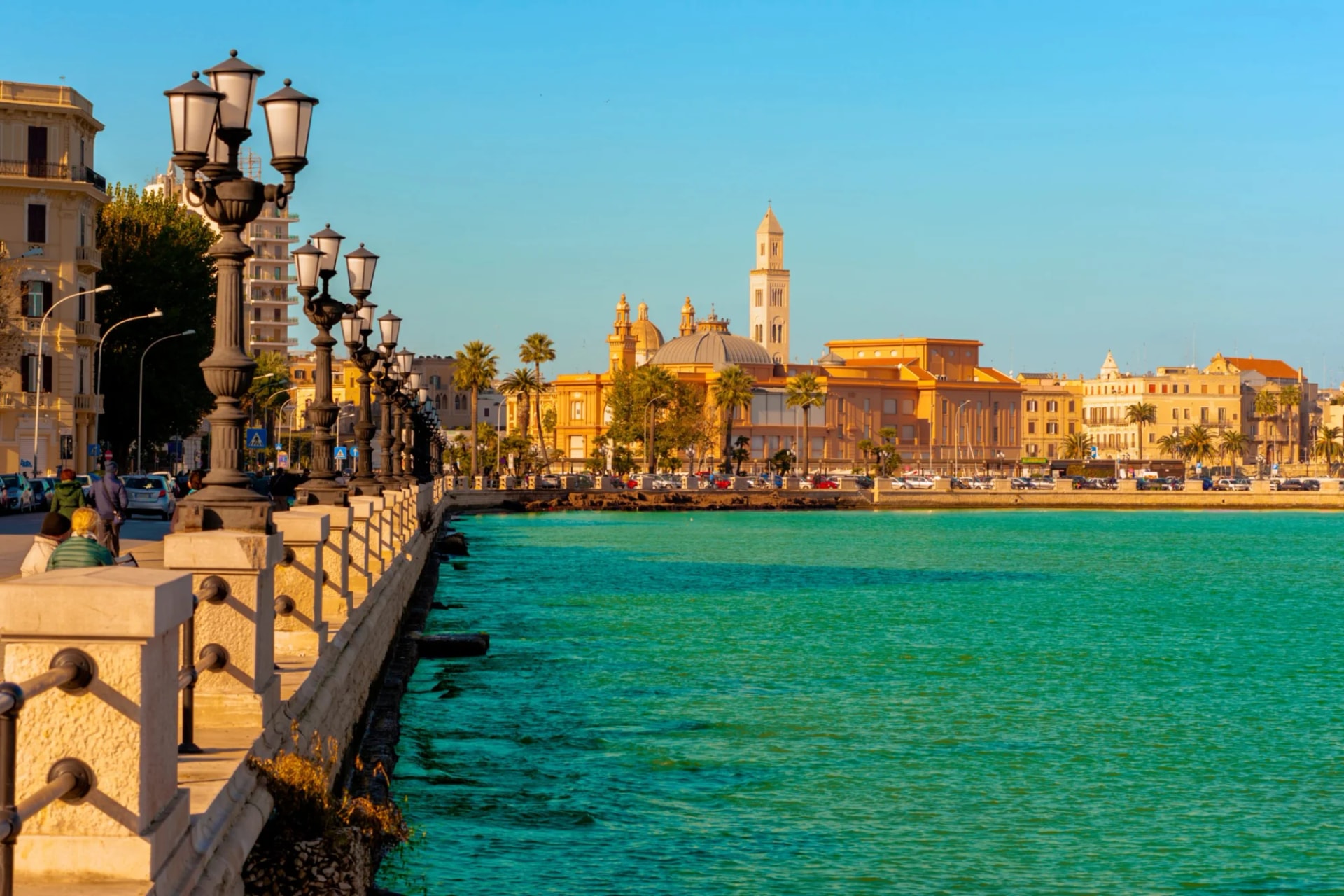 Waterfront promenade with ornate lampposts overlooking turquoise sea and city buildings in Bari.