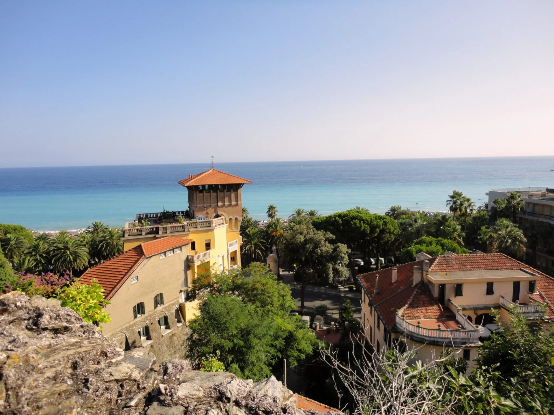Coastal view of colorful buildings, palm trees, and the bright blue sea in Finale Ligure.