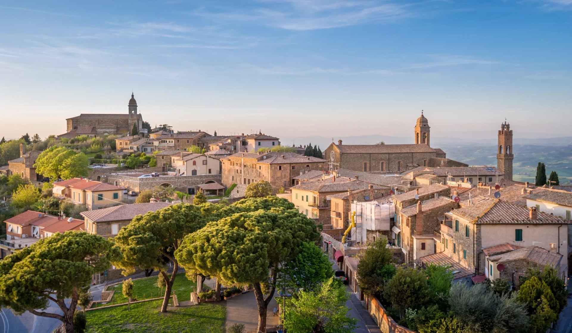 Historic hilltop town of Montalcino, Italy, with stone buildings and church towers under a blue sky.
