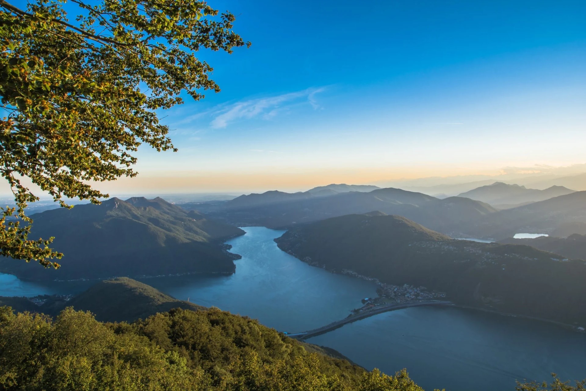 Lake and mountain panorama at sunset, viewed over green foliage, likely Balcone d'Italia.