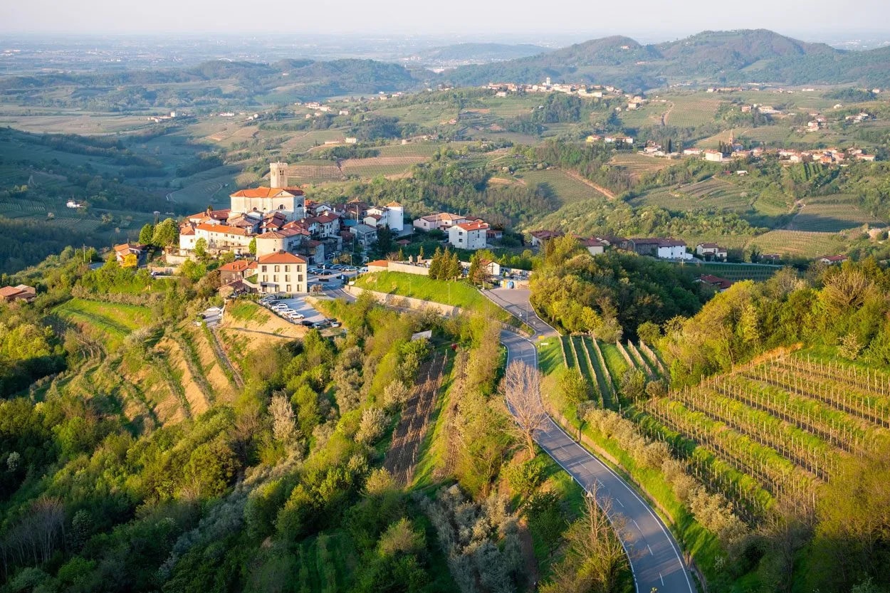 Hilltop village in Goriška Brda with vineyards and winding road in green rolling hills.