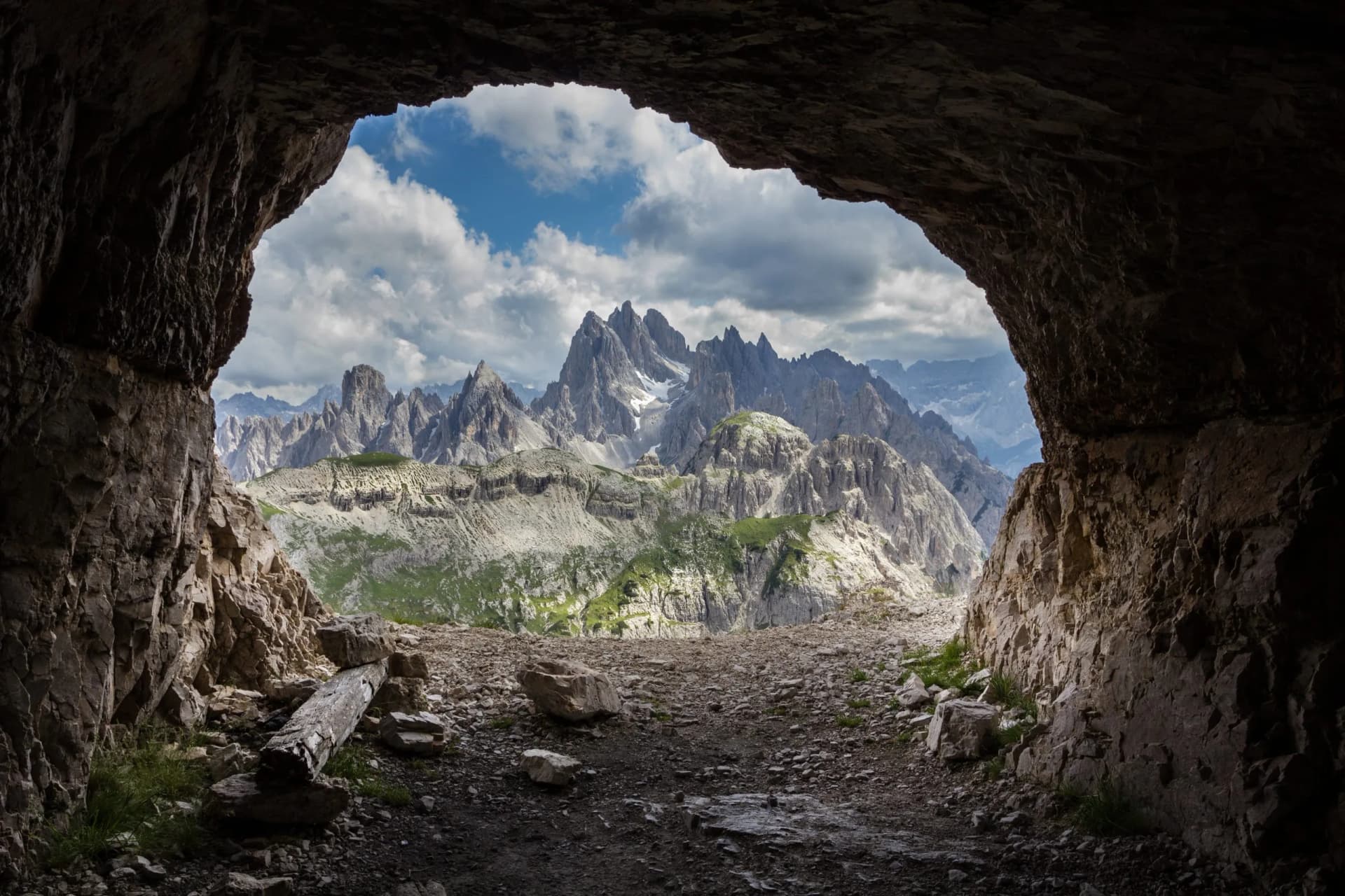View of jagged, rocky Dolomites mountains from inside a dark cave entrance.