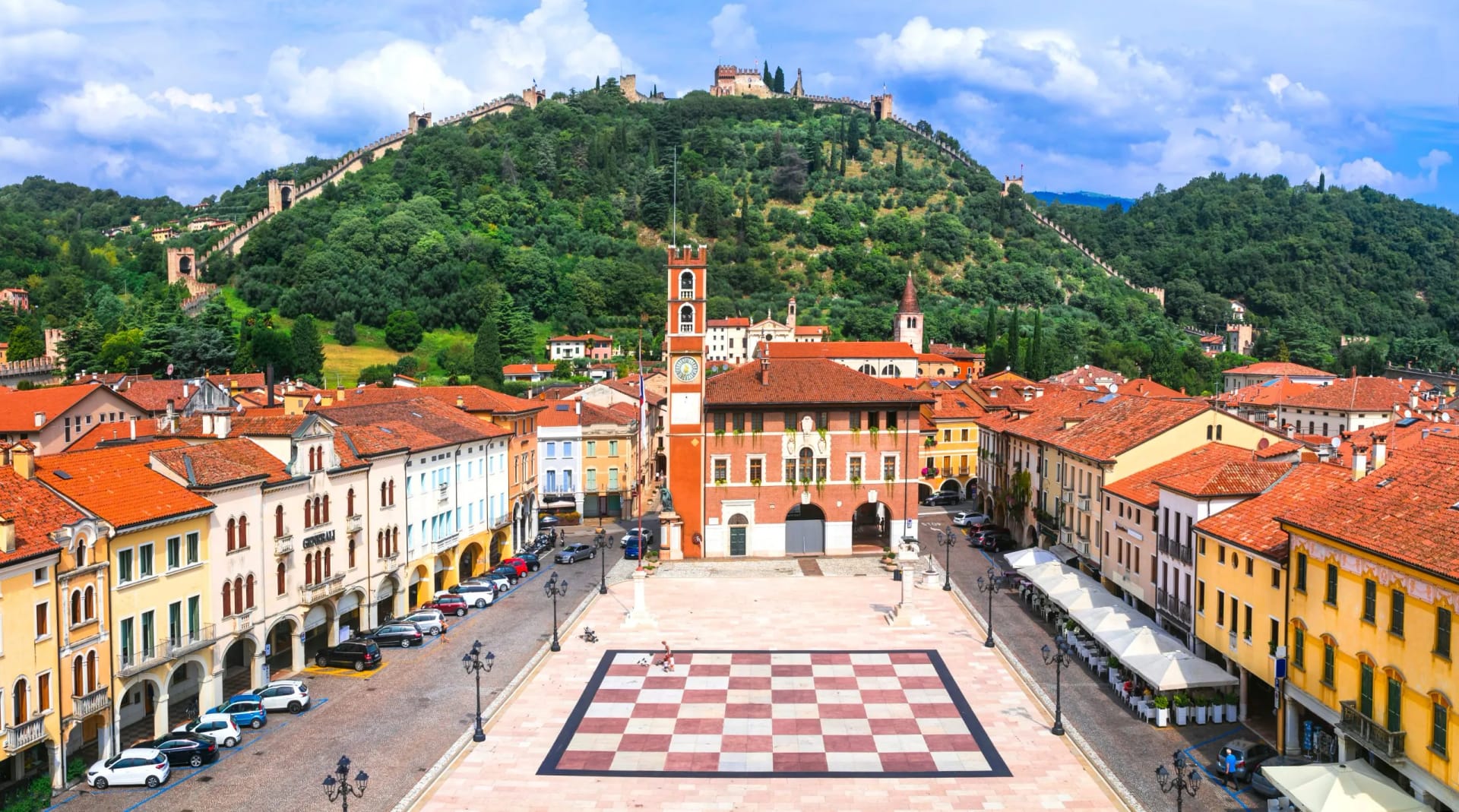 Historic town square with giant chessboard, clock tower, and fortified hill in Veneto, Italy.