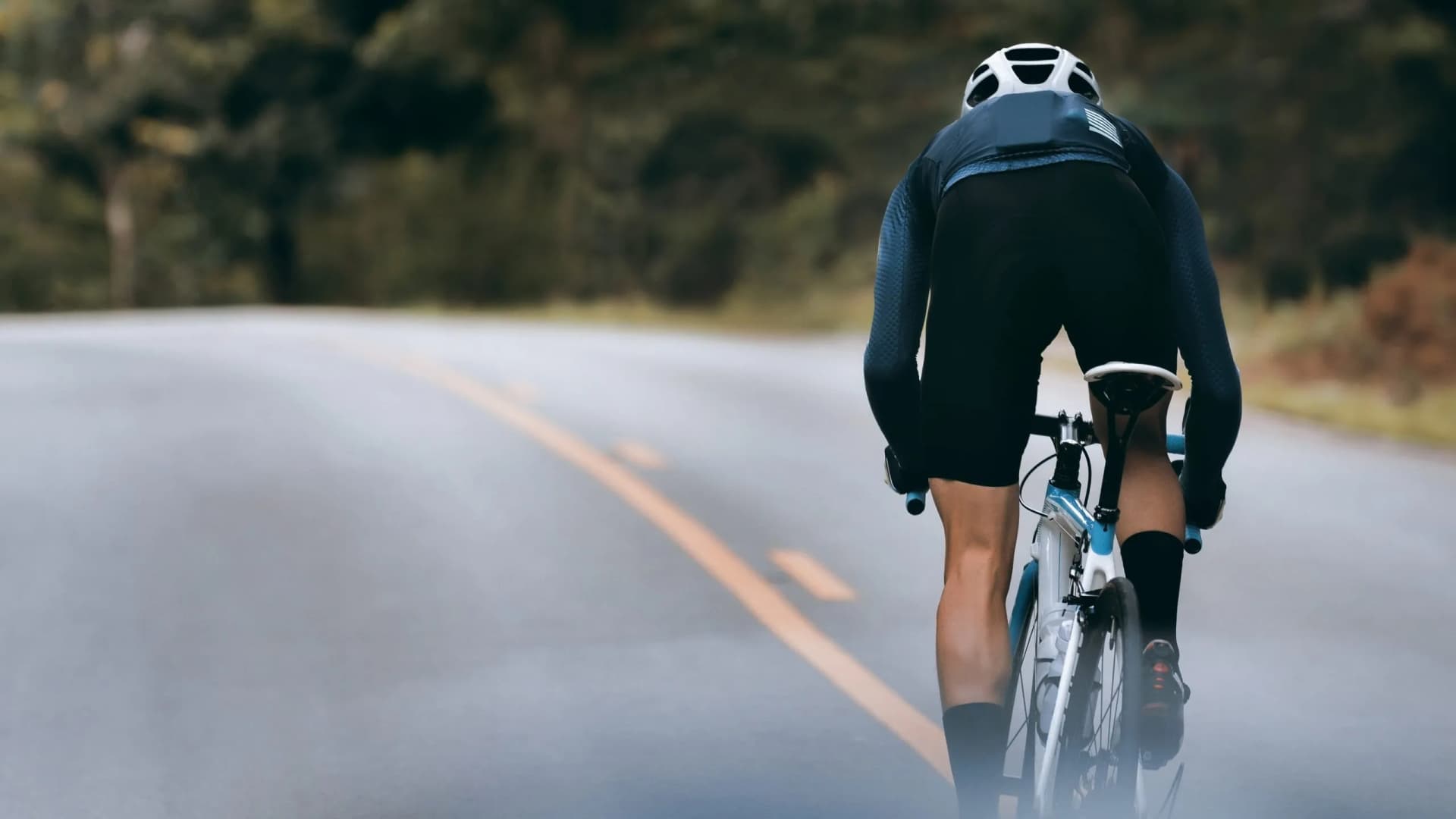 Cyclist in helmet riding on paved road through forested area in Italy