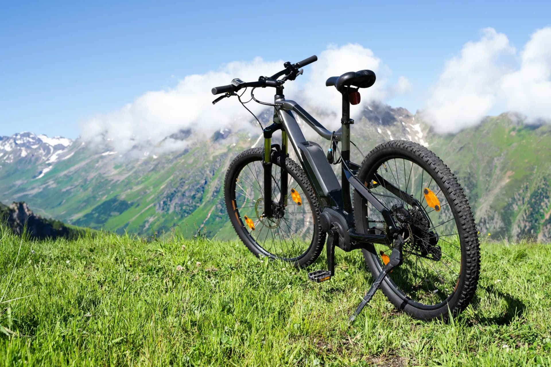 E-bike parked on grassy mountain meadow with green slopes and snowy peaks in background