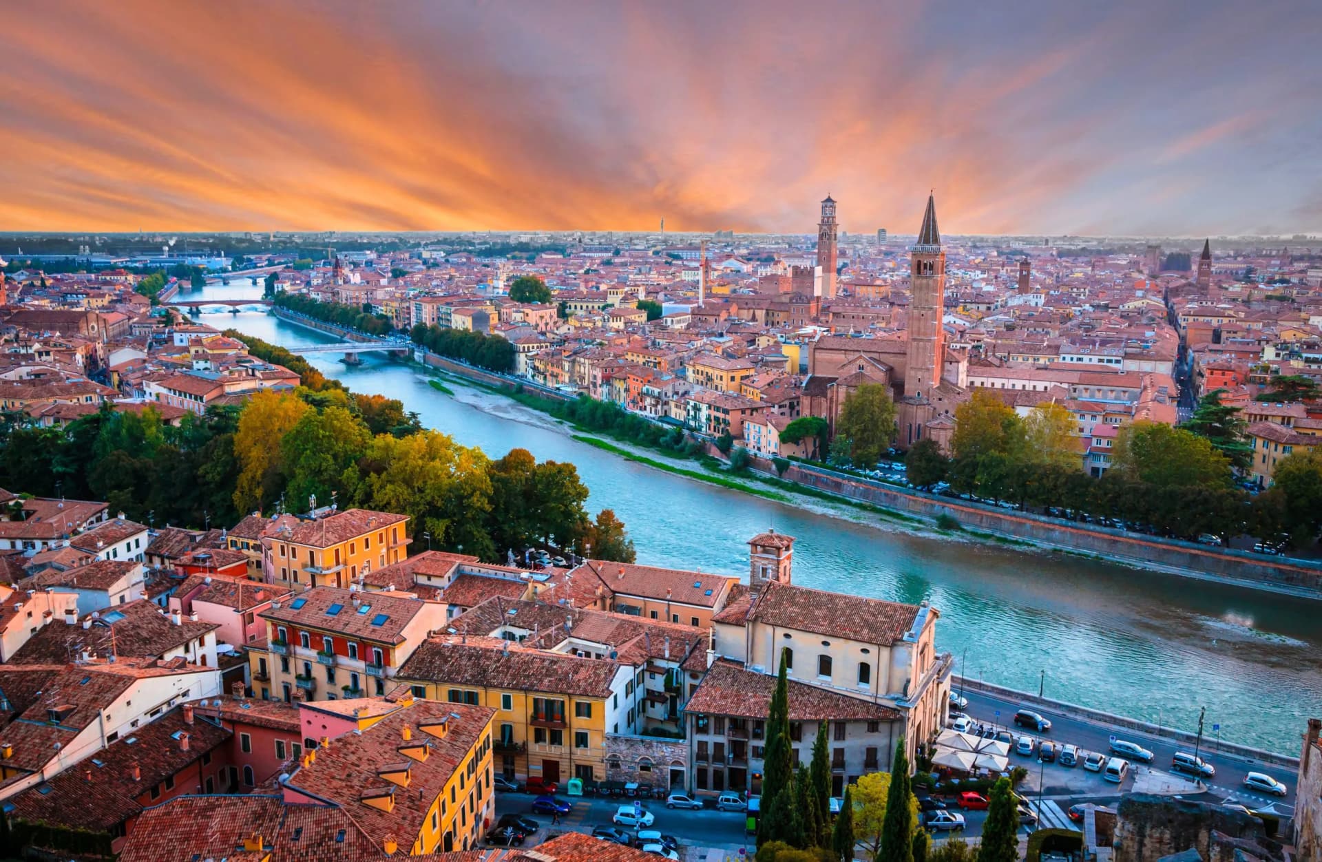 Verona cityscape with terracotta roofs, Adige River, and dramatic sunset sky.