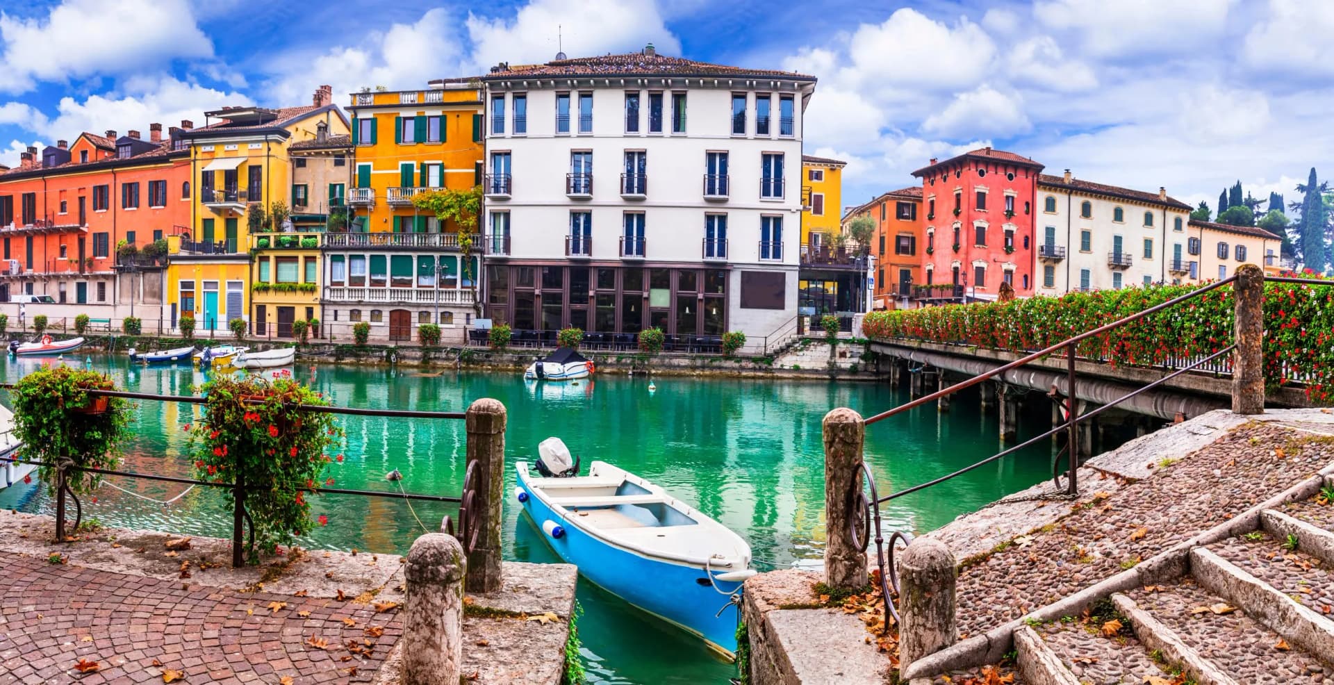Blue boat docked on canal next to colorful buildings in Peschiera under blue sky.