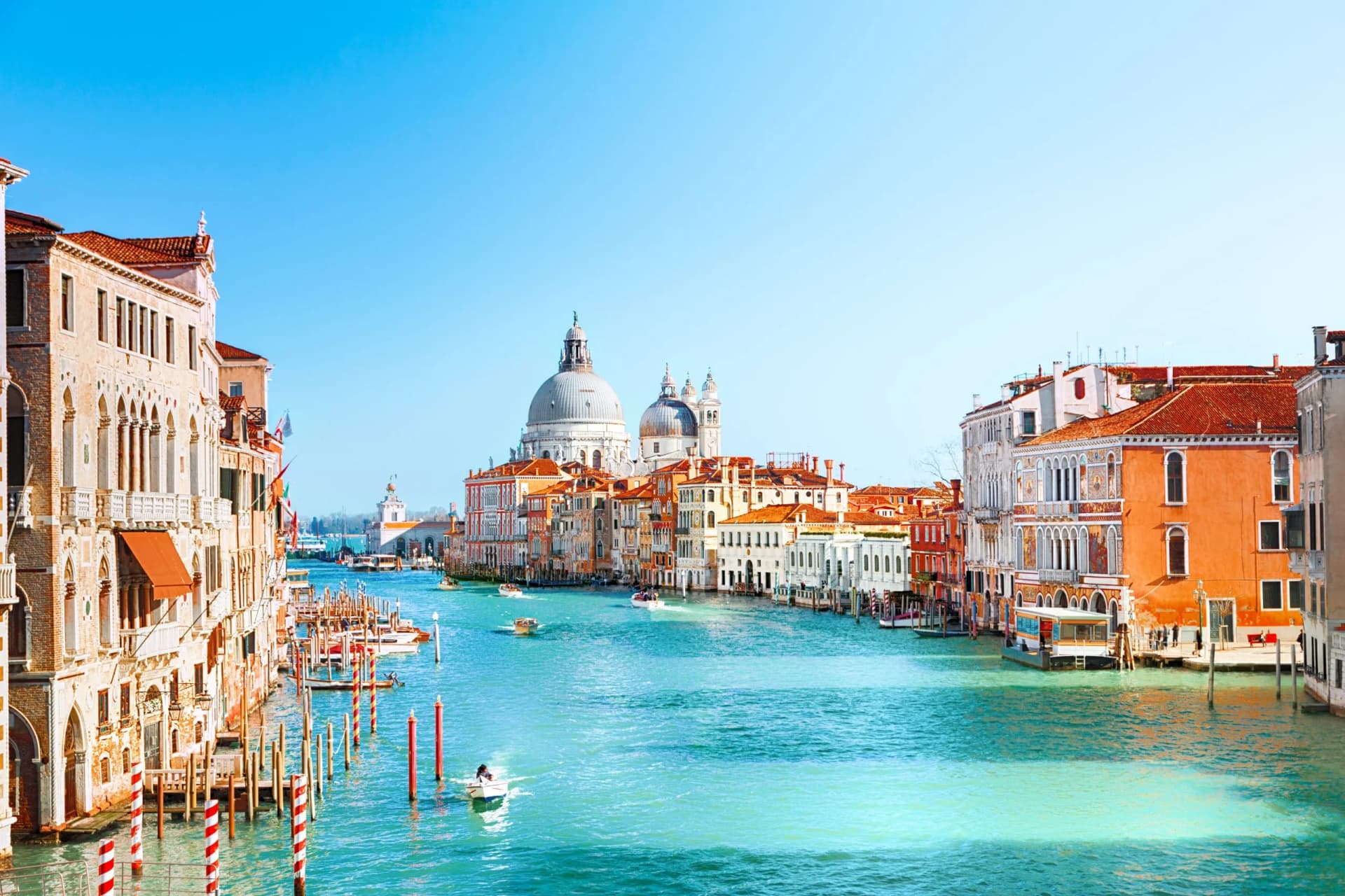 Boats navigate the Grand Canal past historic buildings and the dome of Santa Maria della Salute in Venice.