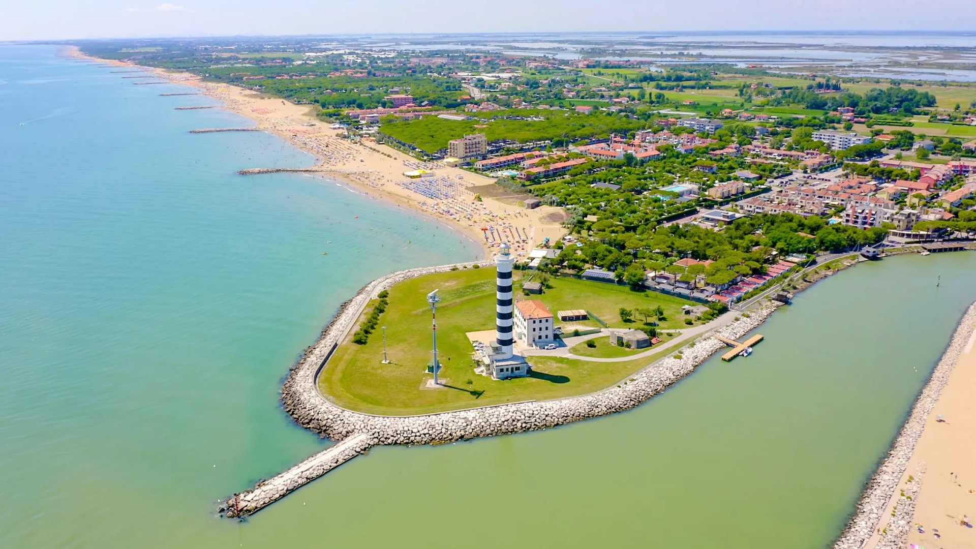 Lighthouse on peninsula next to crowded beach and green lagoon in Jesolo.