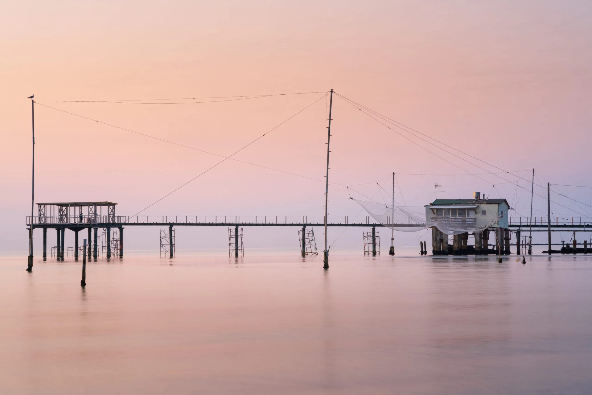Fishing huts with nets on stilts over calm water at sunrise or sunset in Venice.