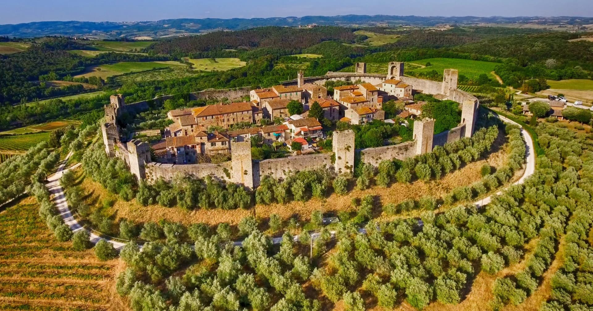 Walled medieval village on a hill surrounded by olive groves and rolling green countryside, Monteriggioni.