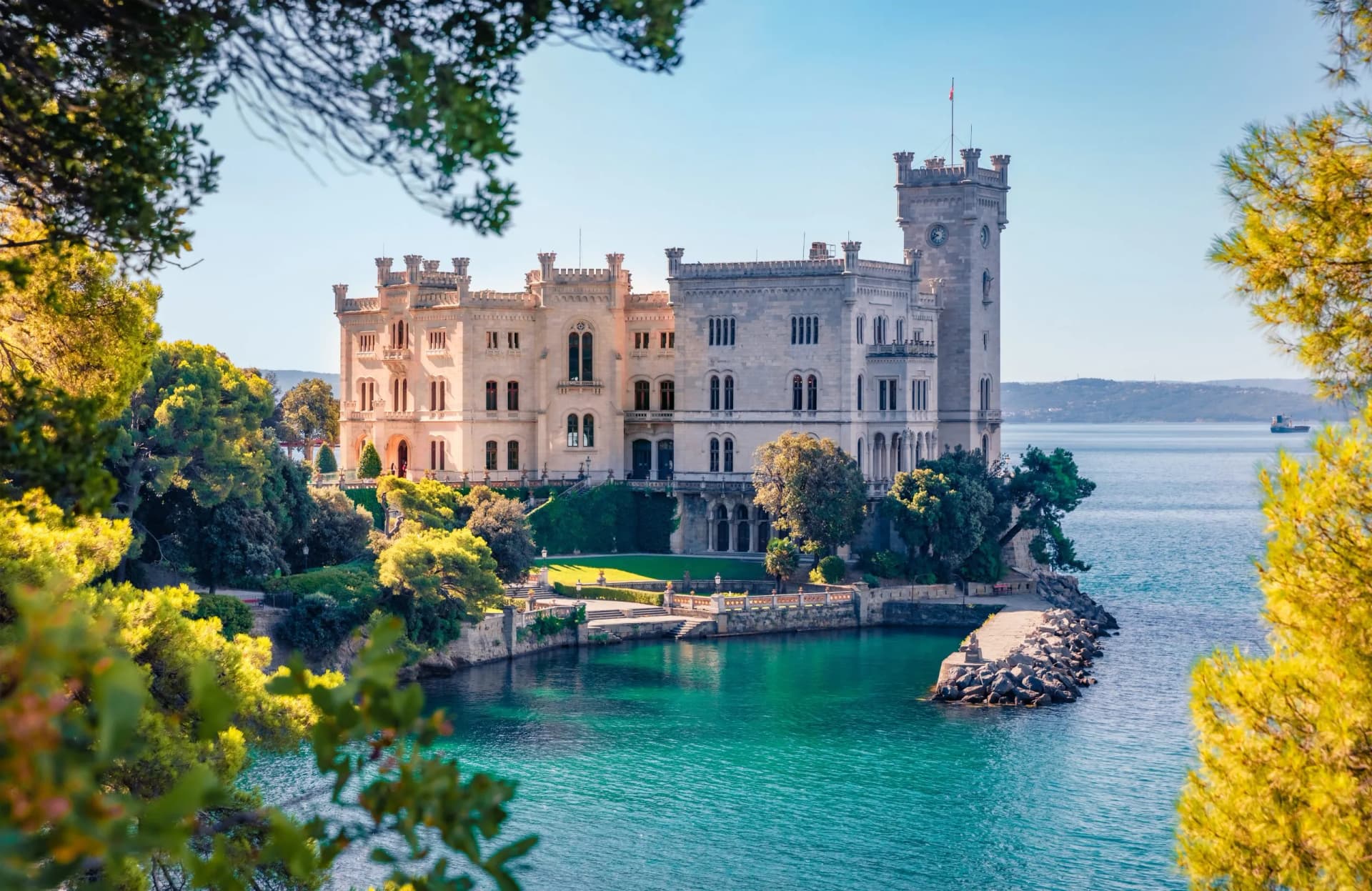 Miramare Castle on the Adriatic Sea framed by sunlit green foliage