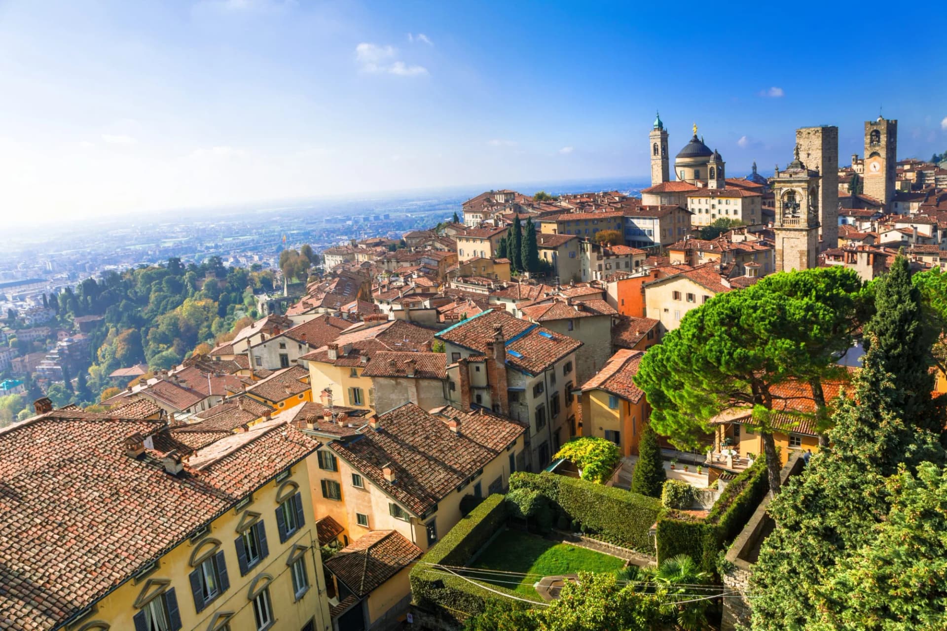 Rooftops of historic buildings in Bergamo overlooking the lower city under a clear blue sky.