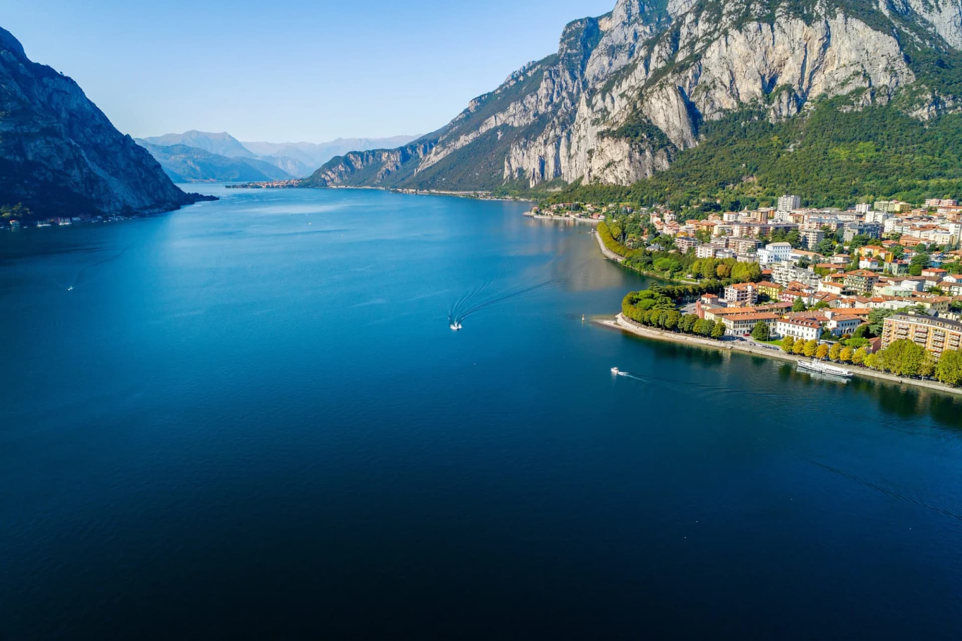 Aerial view of Valsassina town on deep blue lake surrounded by steep mountains.