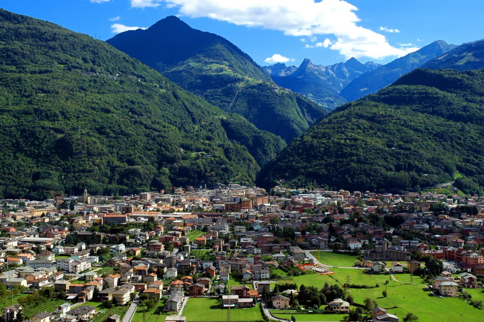 Town nestled in a valley surrounded by steep, forested mountains under a blue sky.