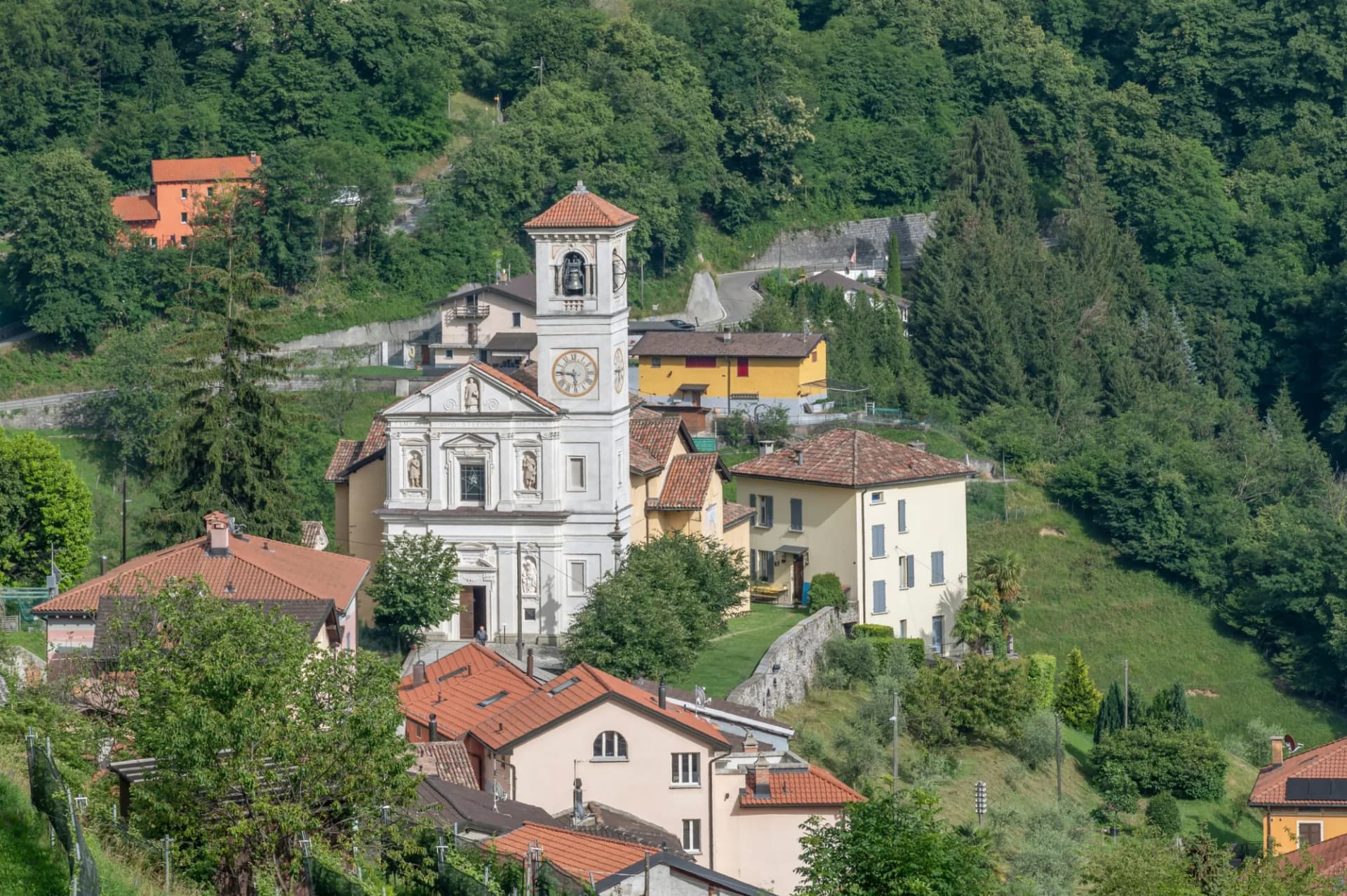 Top view of the Church of Santo Stefano in Arogno, Switzerland, surrounded by green hills.