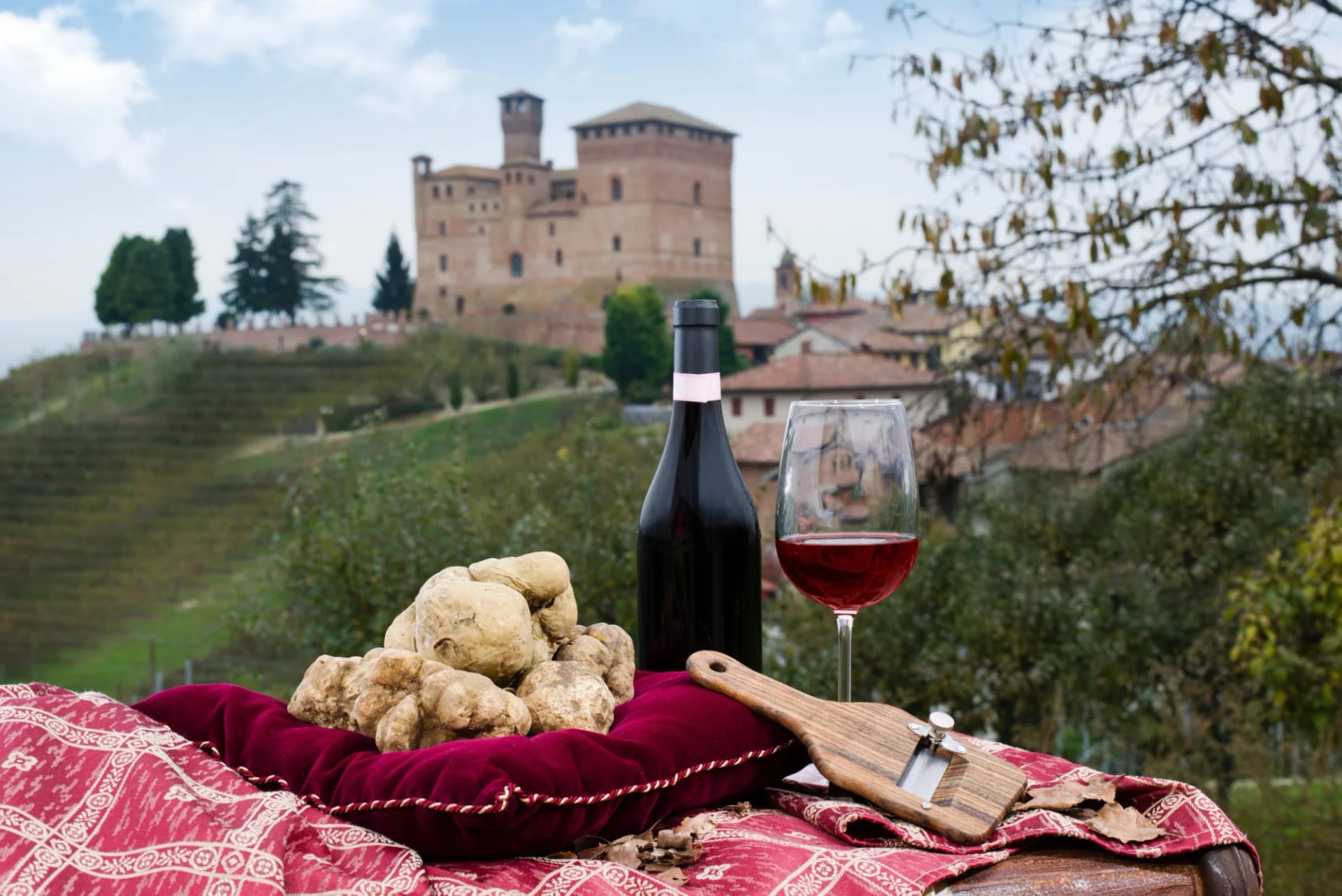 White truffles, red wine, and a truffle slicer with a castle in Piedmont, Italy background.