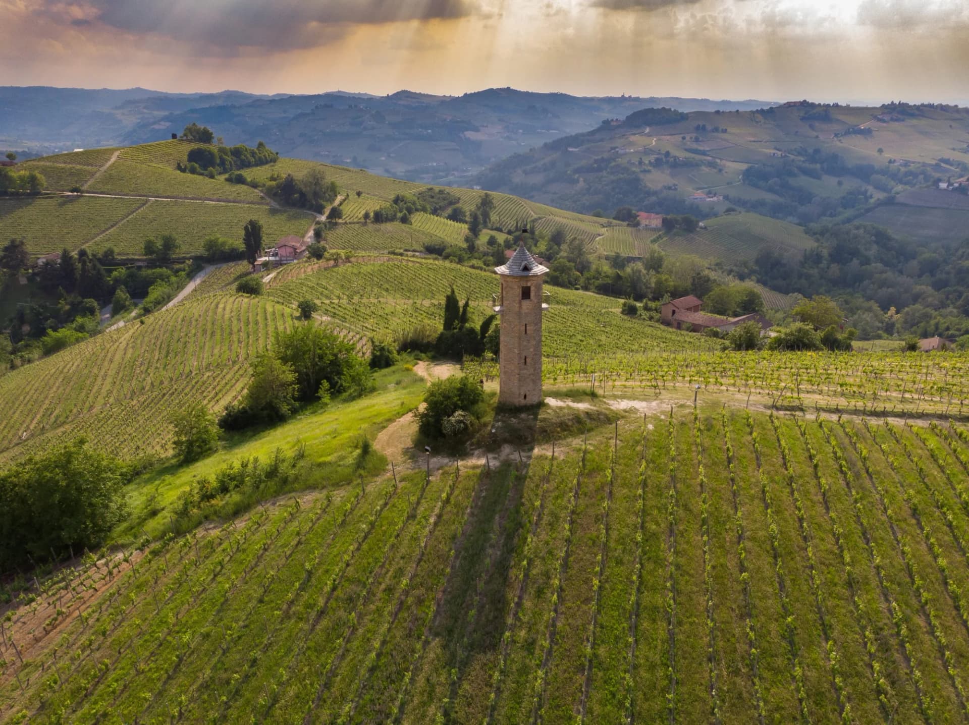 Tower of Contini in Canelli vineyards, Piemonte, Italy, surrounded by rolling green hills under dramatic sky.