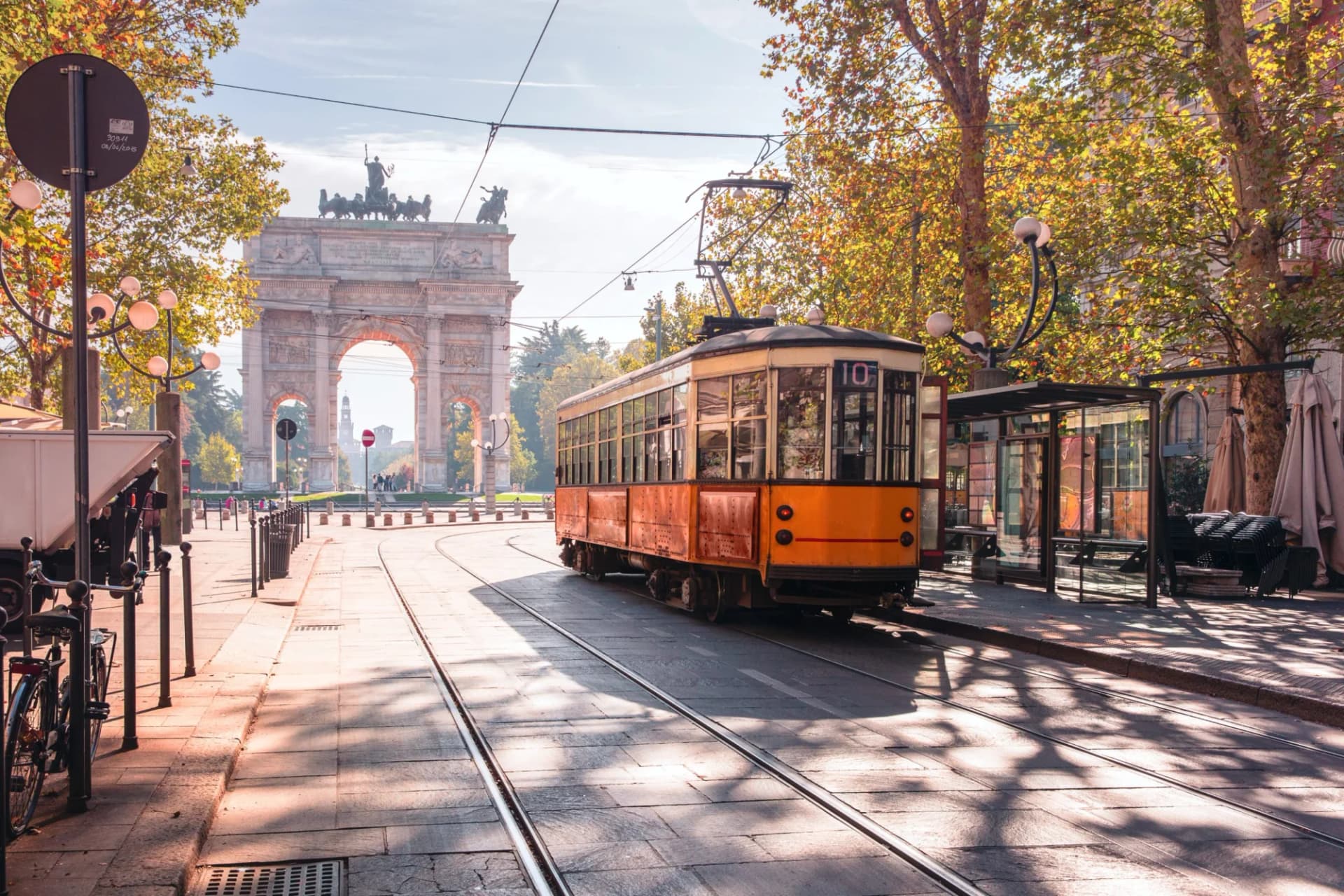Vintage orange tram in Milan old town center near Arco della Pace with autumn trees.