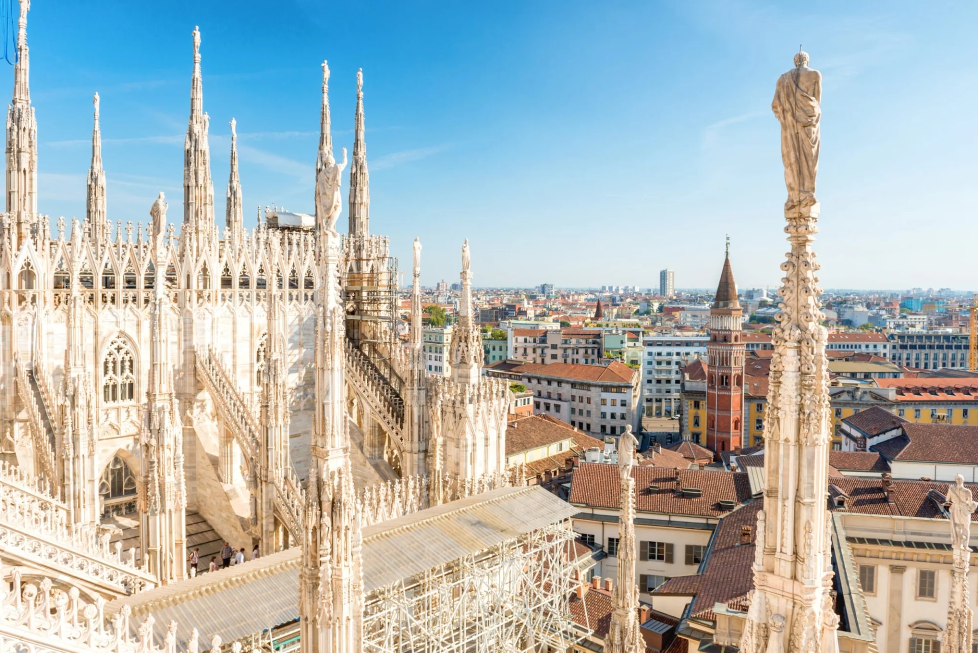 White marble spires and statues atop the Duomo cathedral with a view over the city of Milan.