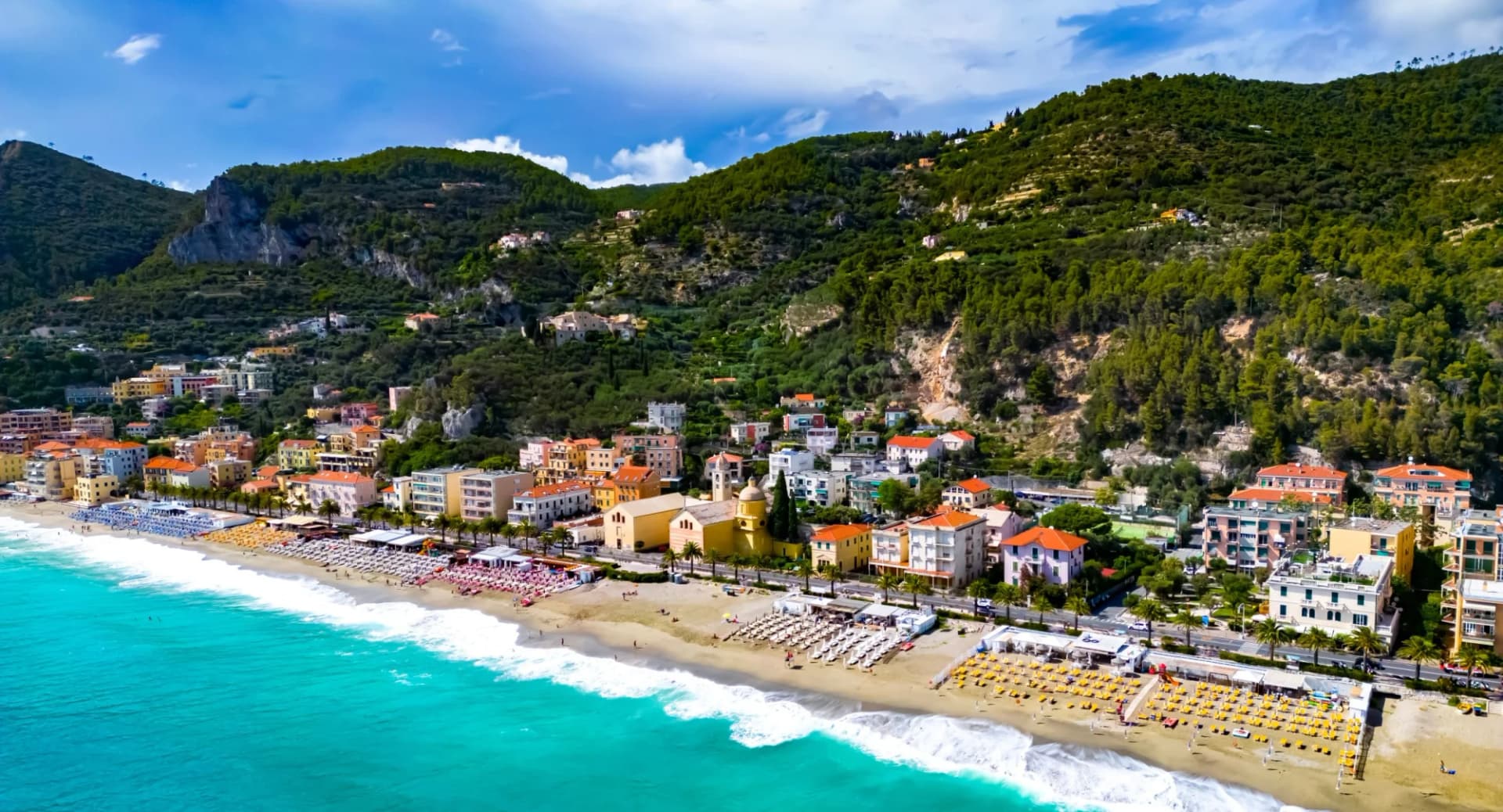 Aerial view of Varigotti beach with turquoise water, colorful buildings, and green hills in Liguria, Italy.