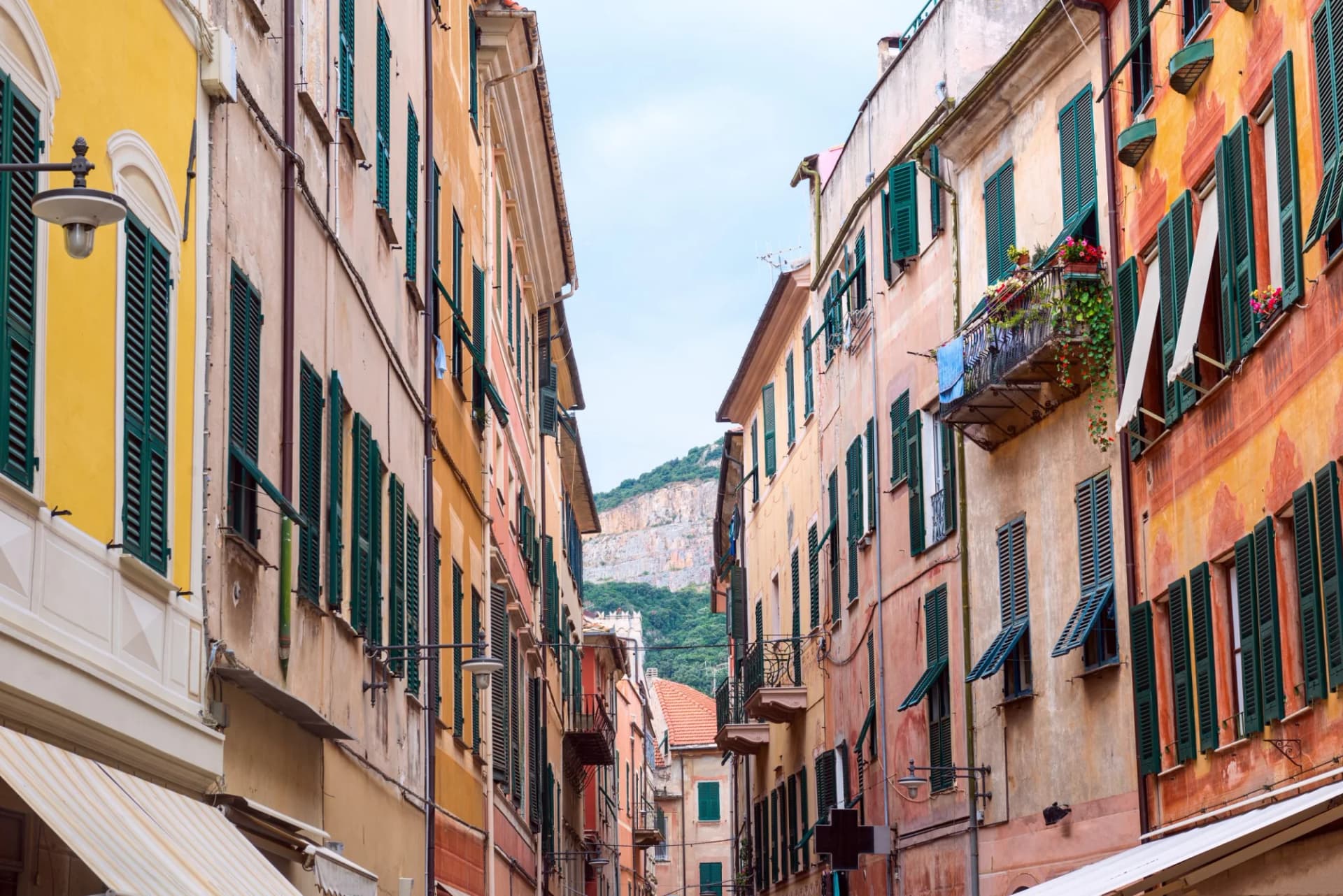 Narrow street in Finale Ligure with colorful buildings and a cliff face visible in the distance.
