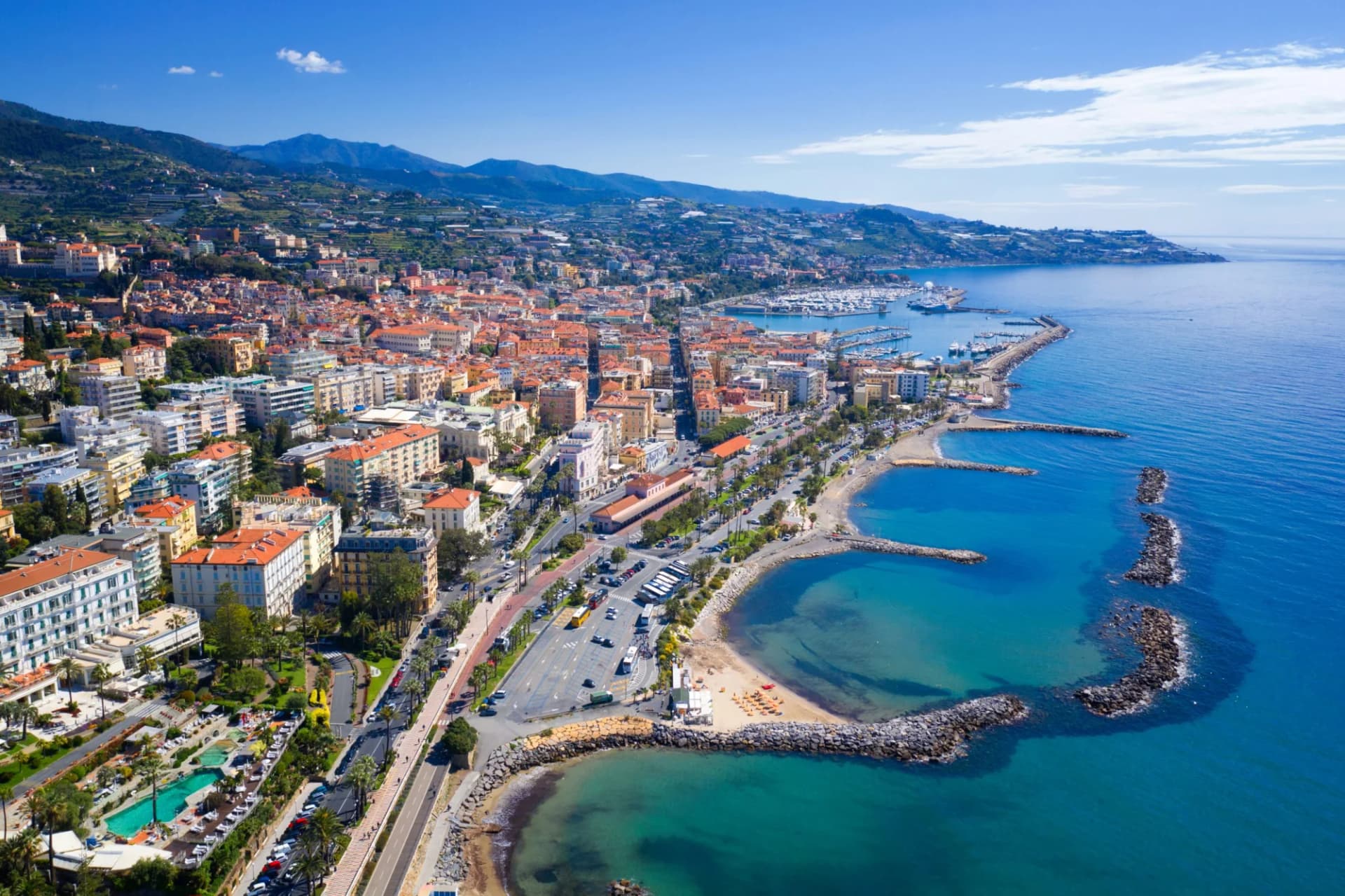 Aerial view of Sanremo coastal city with buildings, harbor, and turquoise Mediterranean Sea.