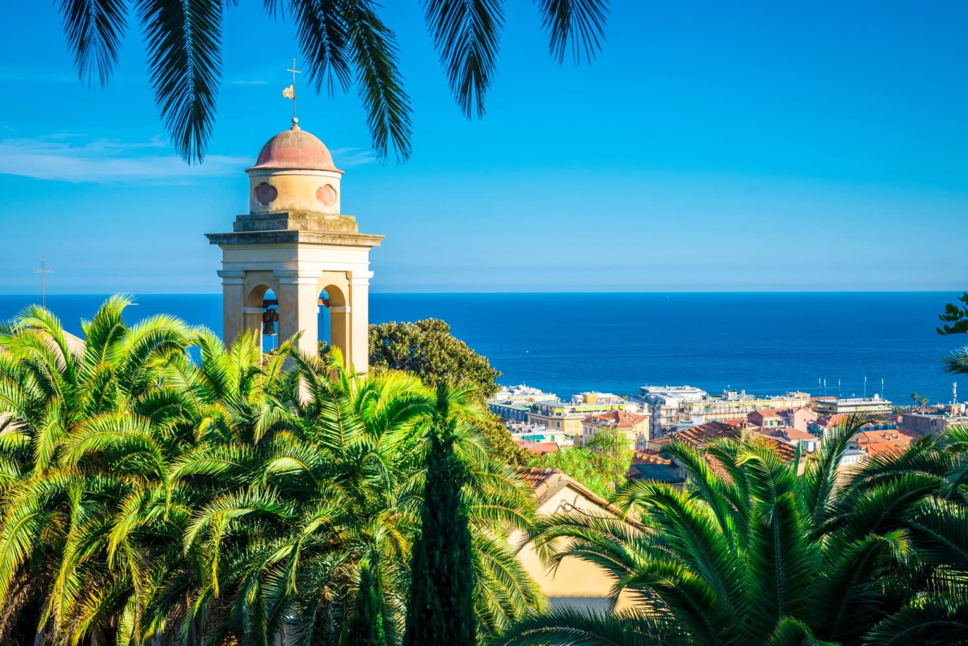 Church belfry above palm trees overlooking the sea and town in Sanremo, Italy.