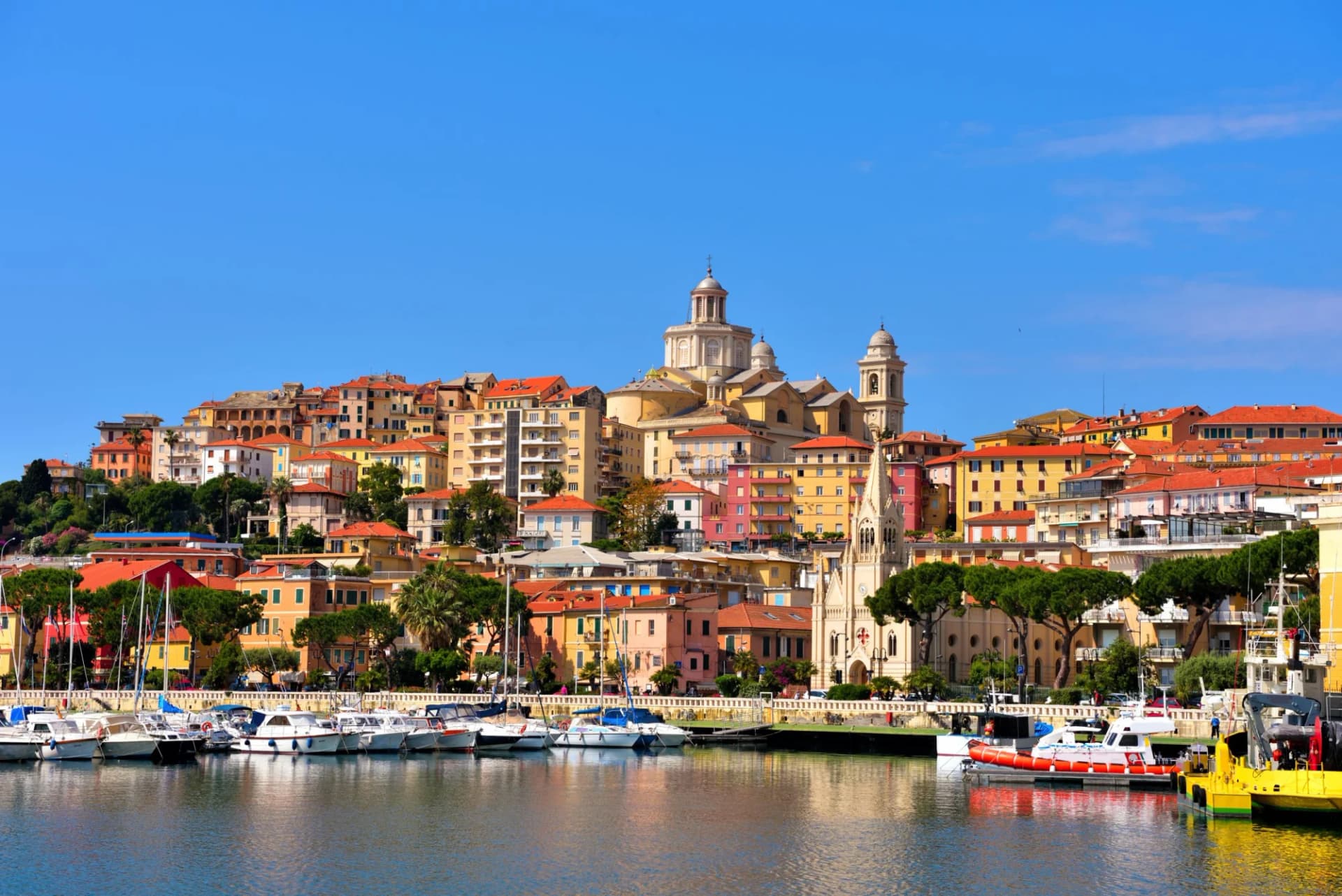 Colorful buildings climb a hill above a harbor with moored boats in Porto Maurizio, Liguria, Italy.