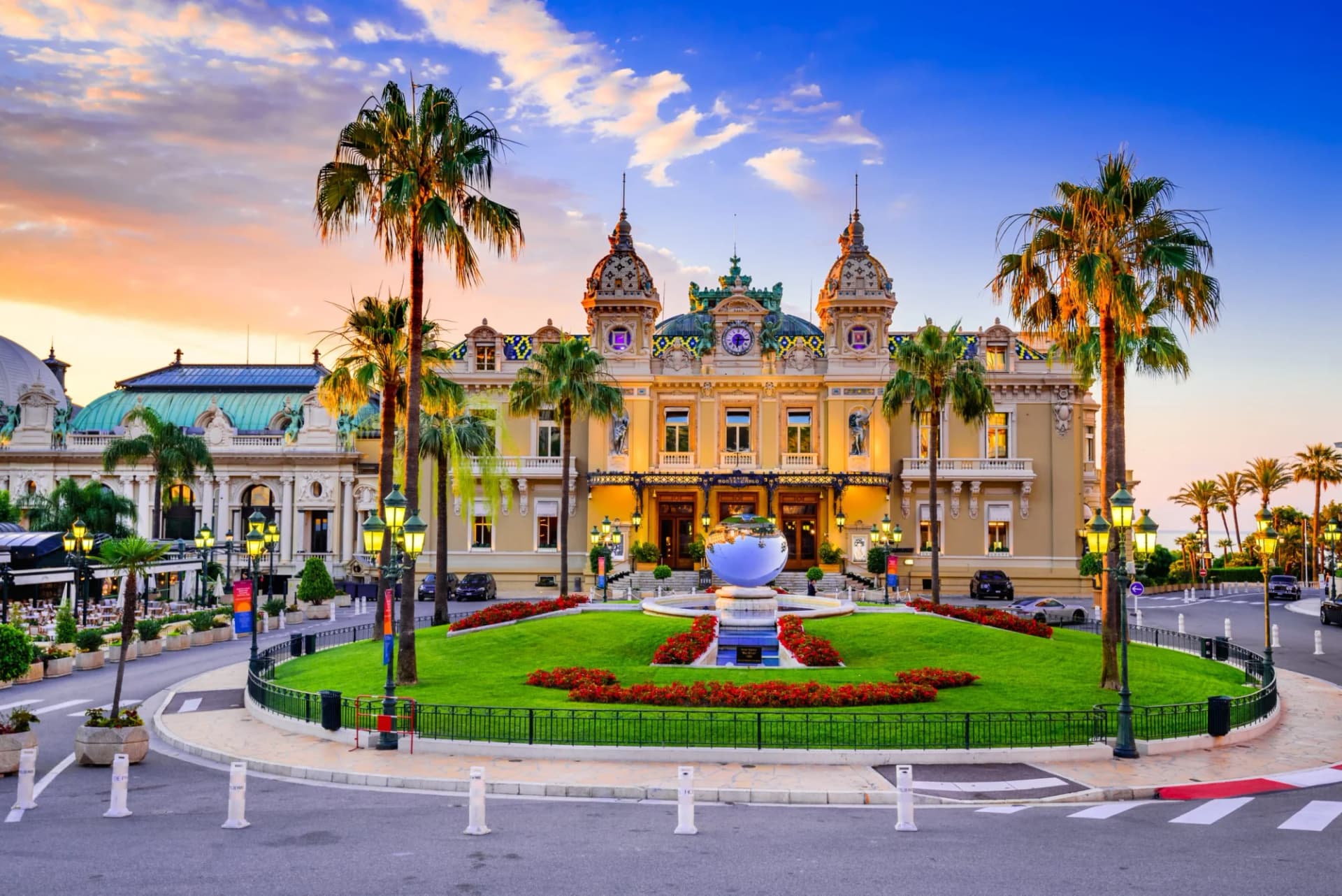 Casino de Monte-Carlo illuminated at sunset with palm trees and a globe fountain.
