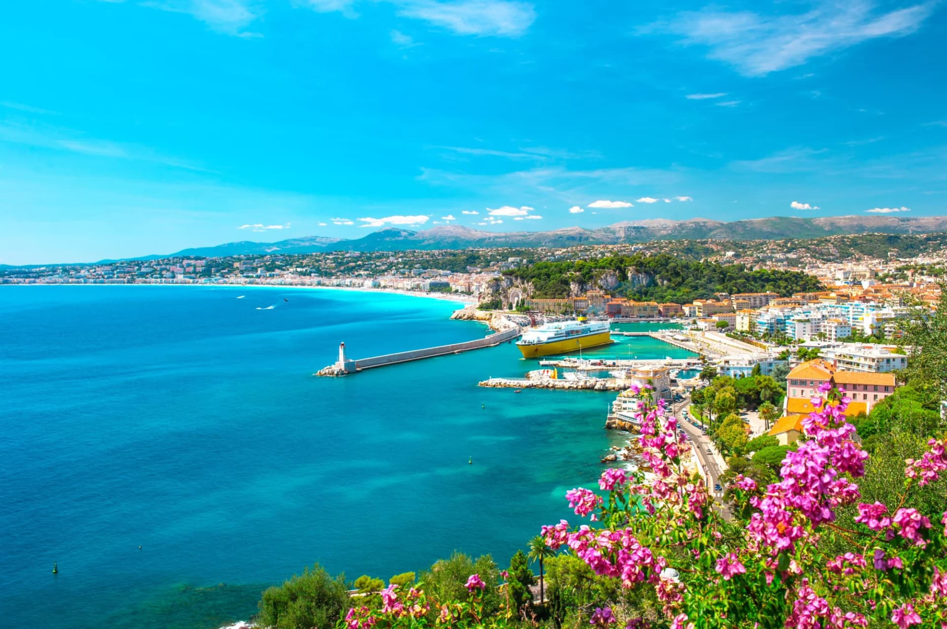 Coastal city with harbor, yellow ship, and pink flowers overlooking the Mediterranean Sea in Nice.