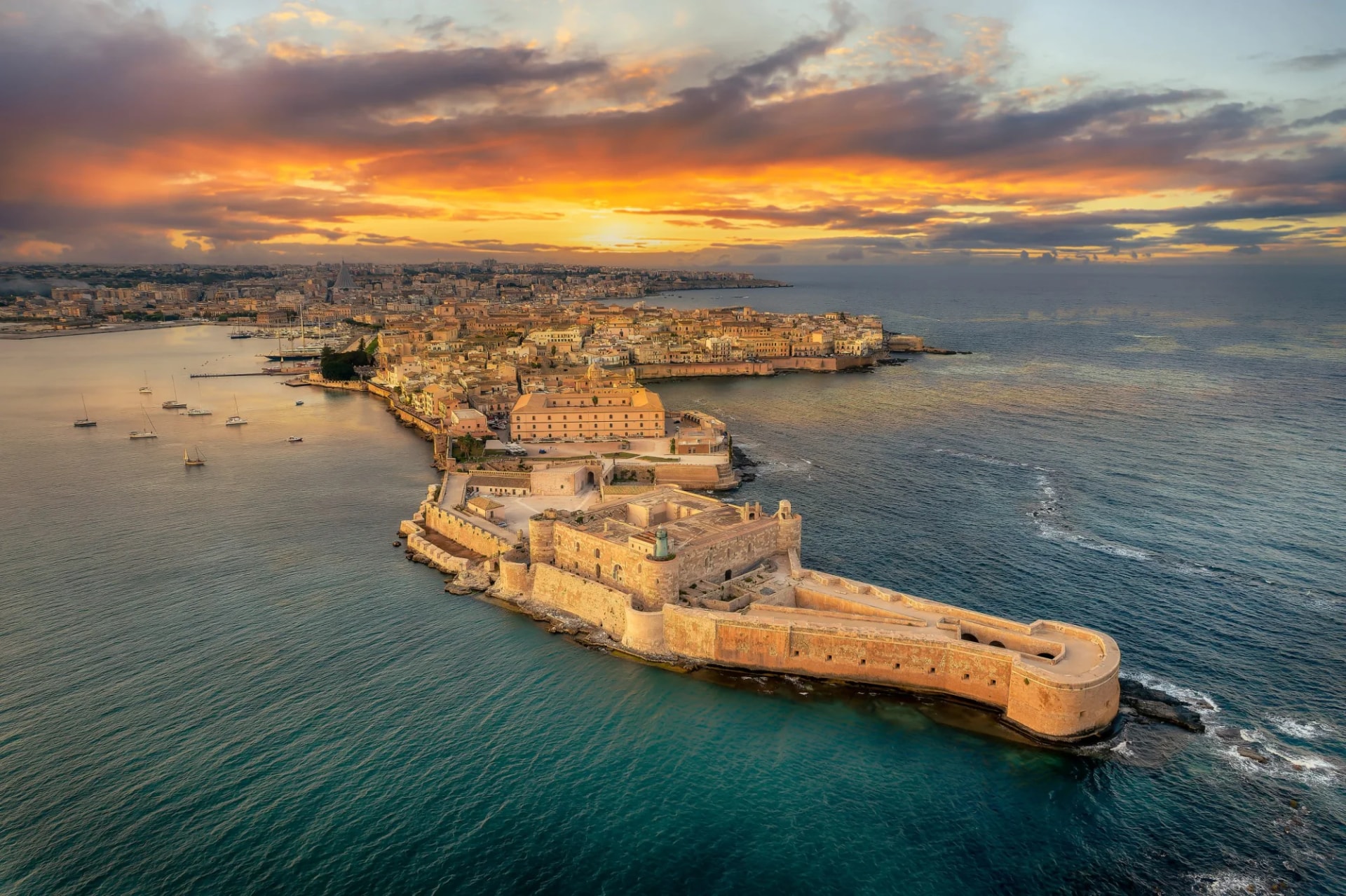 Syracuse fortress and city at sunset over the sea with boats in Sicily, Italy.