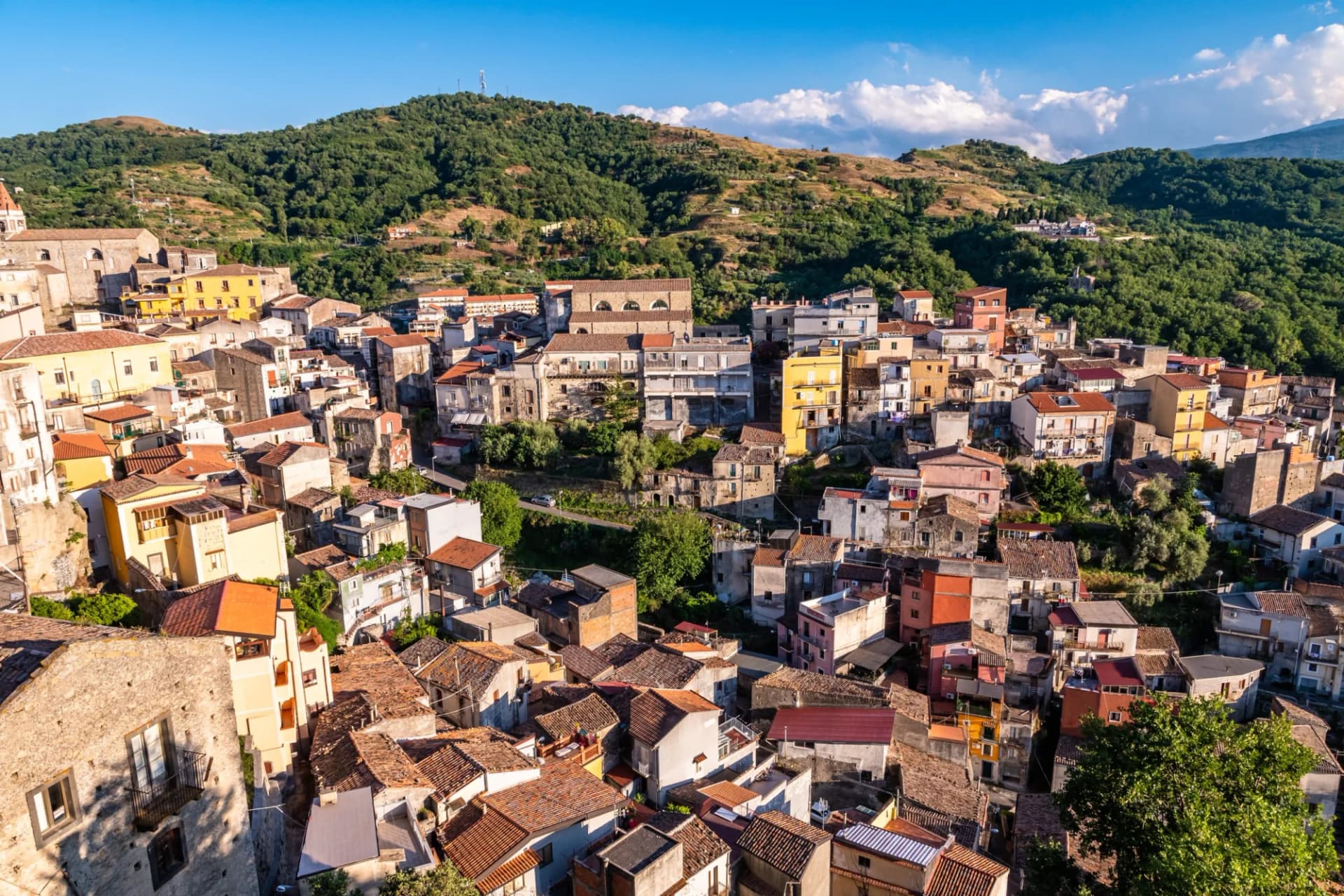 Panoramic view of Castiglione di Sicilia town nestled on a green hillside on a sunny summer day.