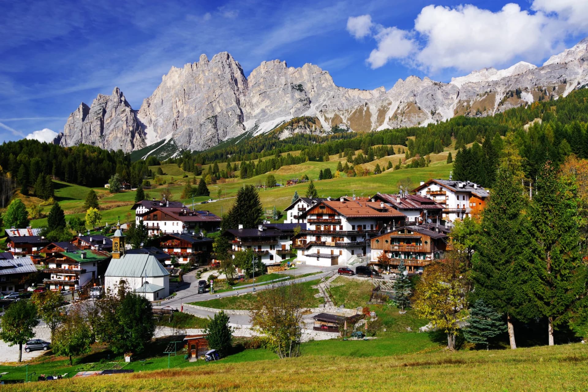 Alpine village with traditional chalets beneath towering gray mountains under a blue sky.