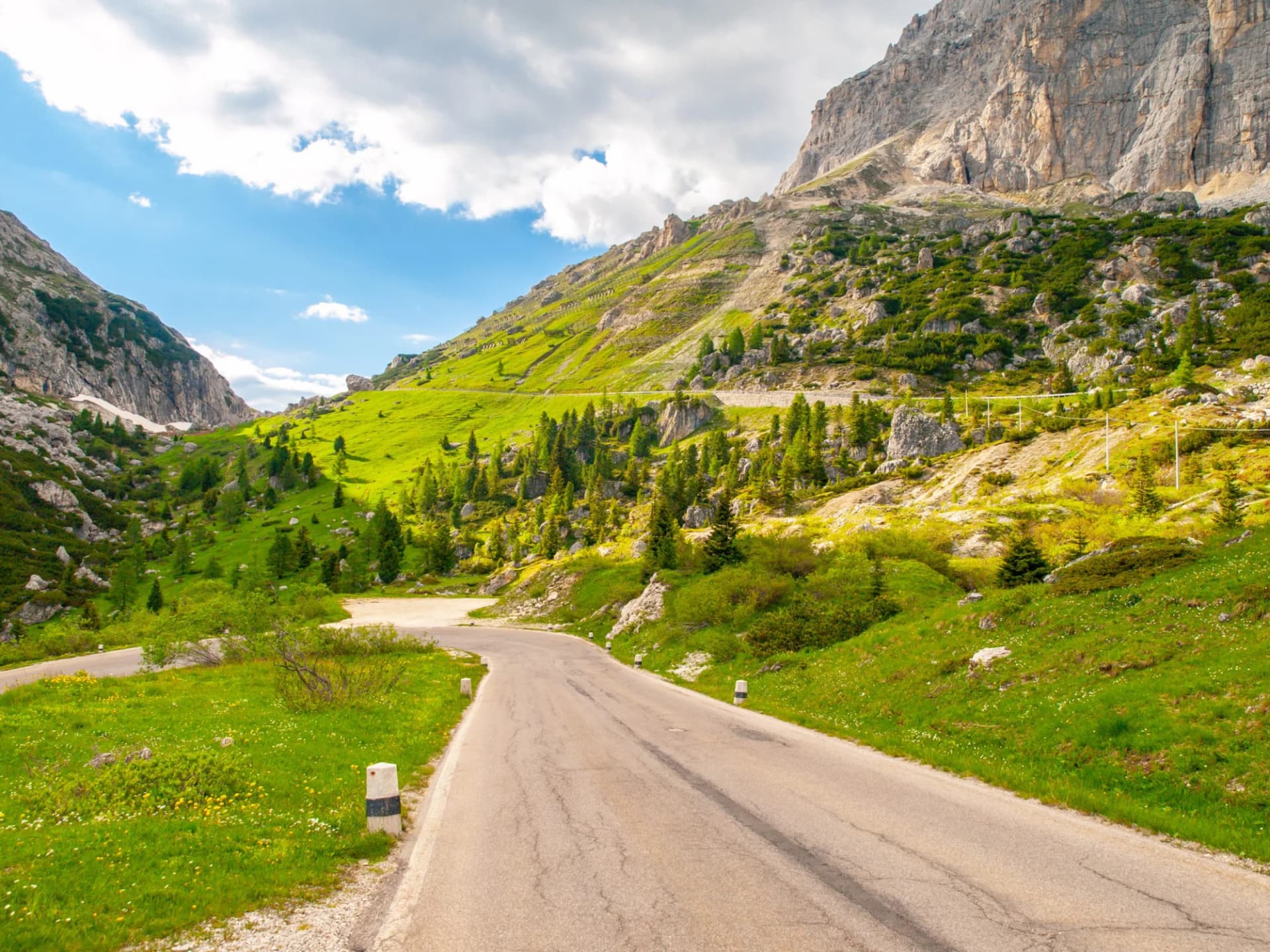 Asphalt road winding through green meadows and dolomite rocks at Passo Falzarego, Italy.