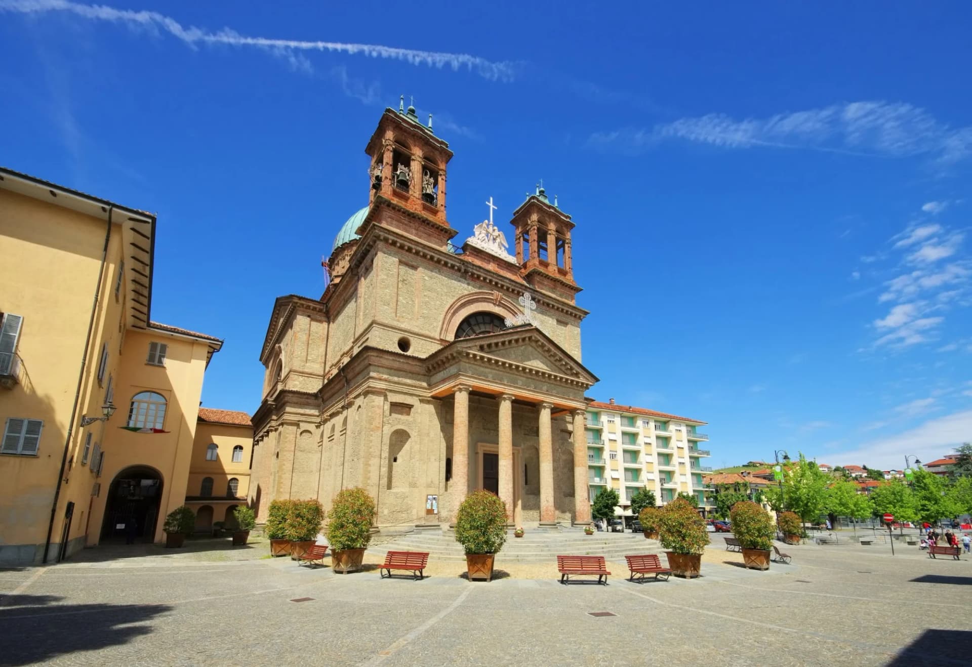 Church with twin bell towers and portico on sunny cobblestone square in Dogliani.