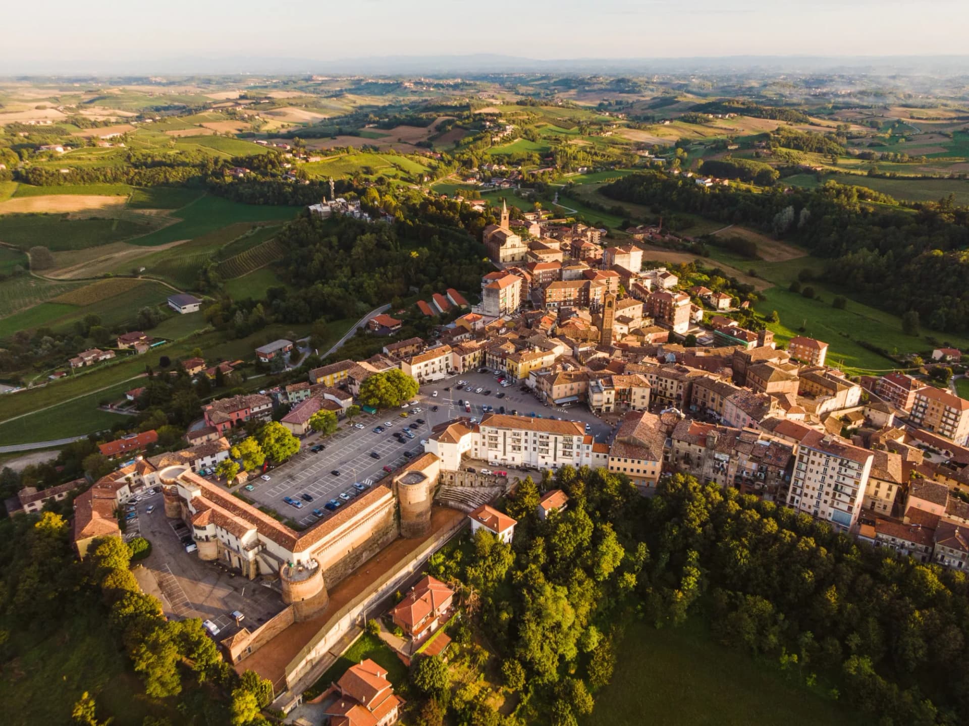 Drone aerial view of Moncalvo Monferrato town on a hill surrounded by green rolling vineyards.