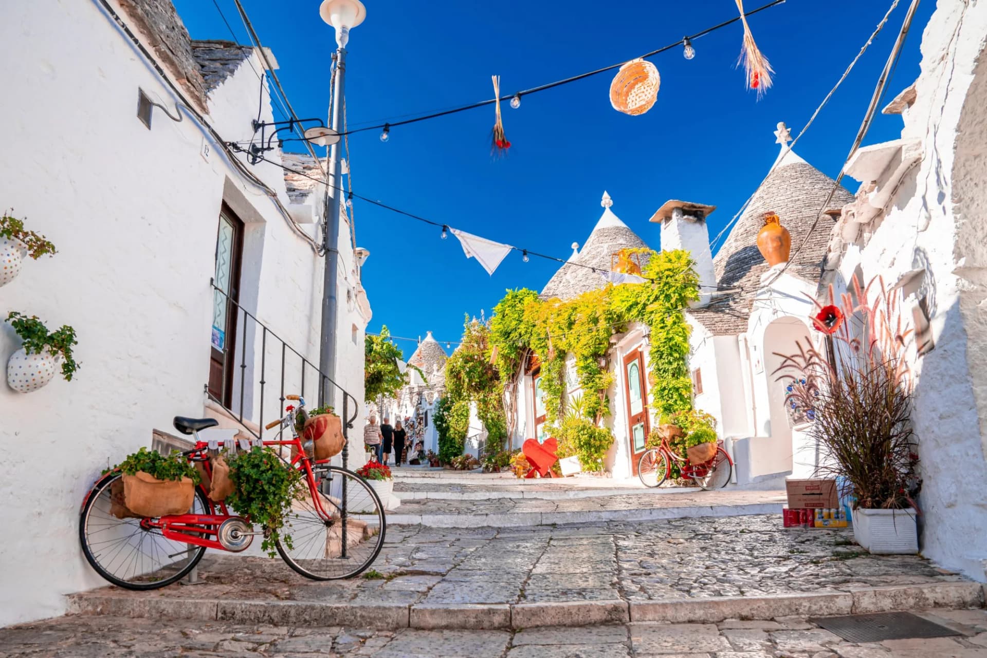 Traditional Trulli houses in Alberobello, Puglia, Italy, with a red bicycle on a stone street.