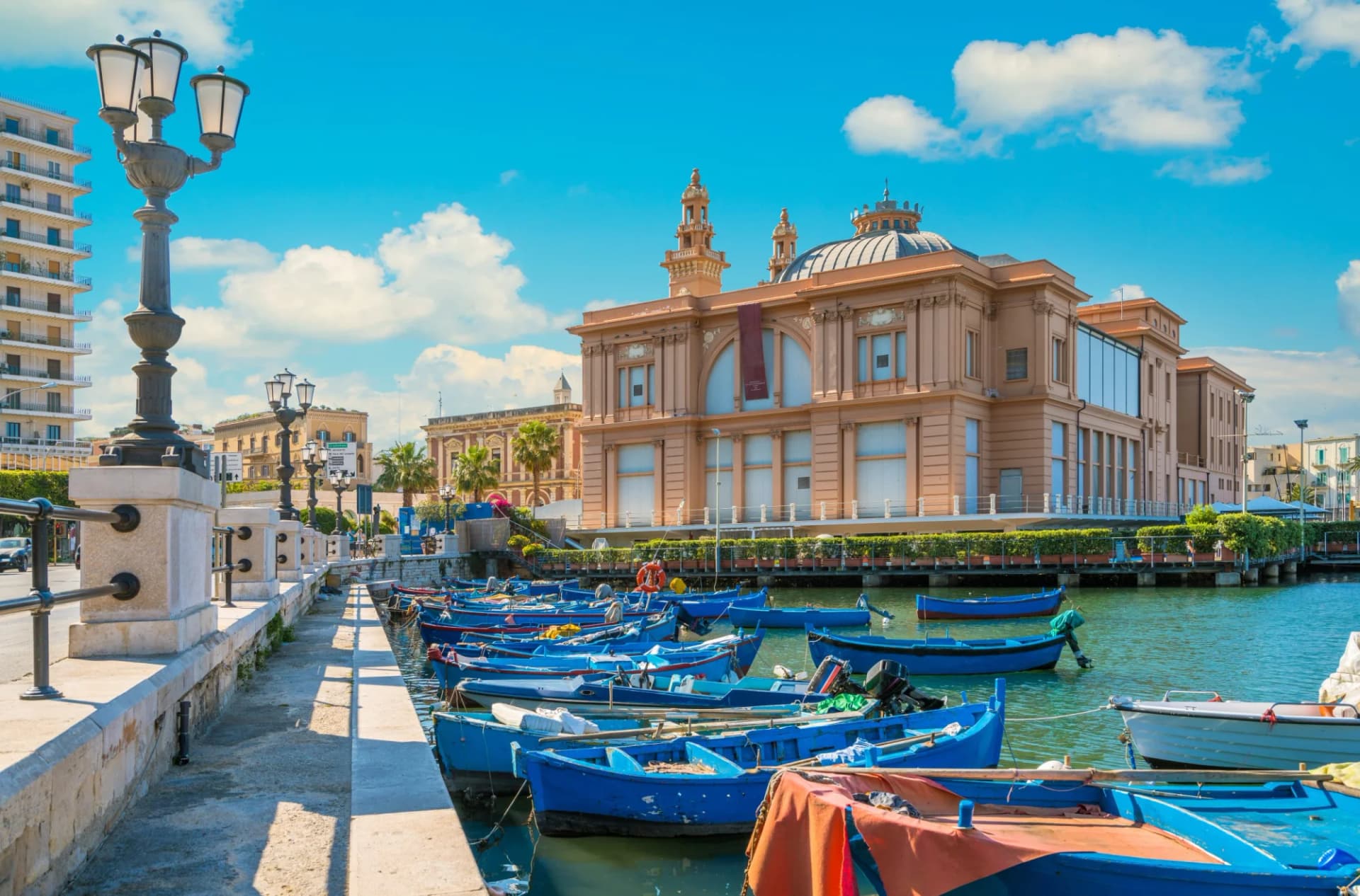 Docked blue fishing boats with the Margherita Theatre in Bari, Apulia, Southern Italy background.
