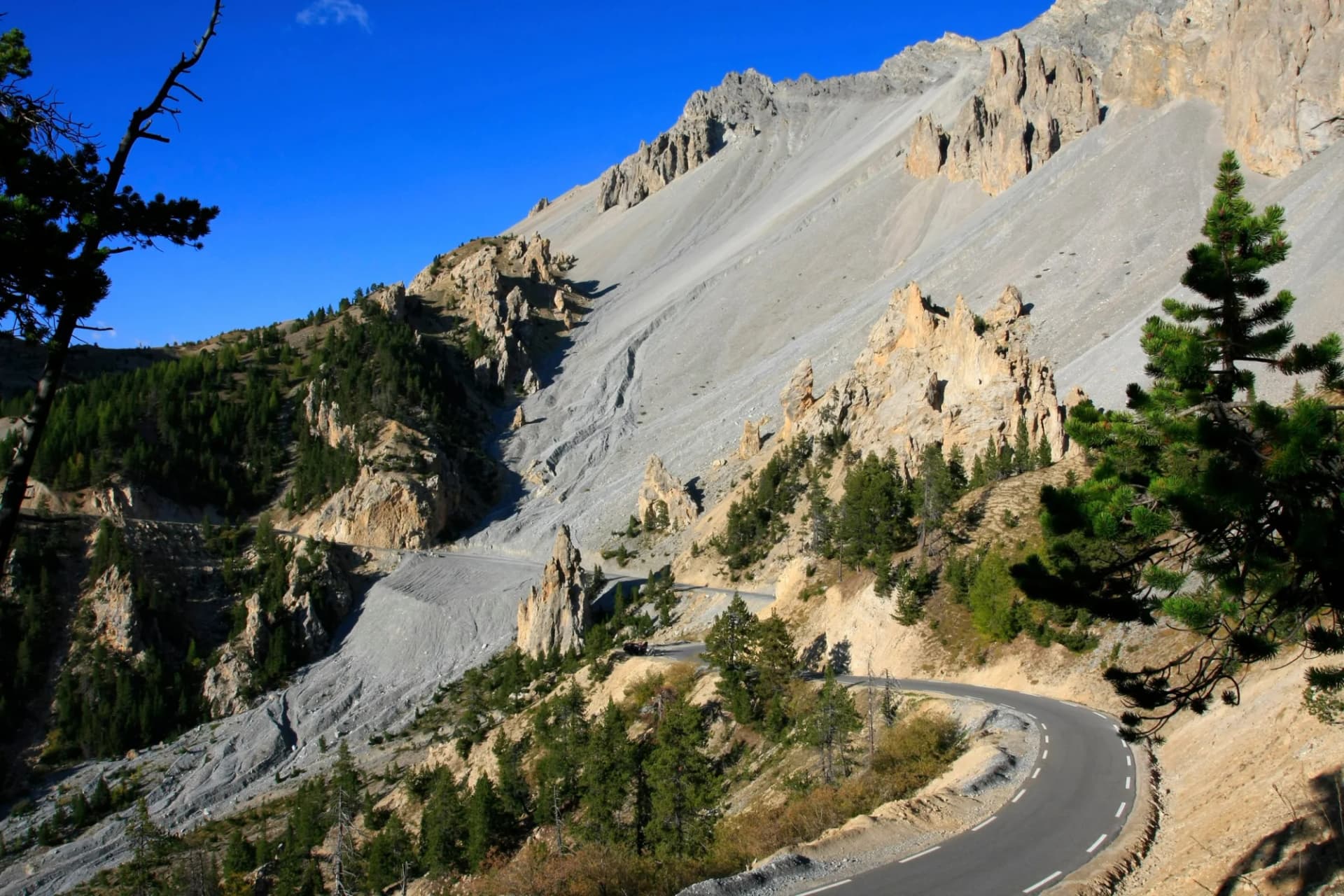 Winding mountain road near steep scree slope and rocky peaks, Col de l'Izoard.