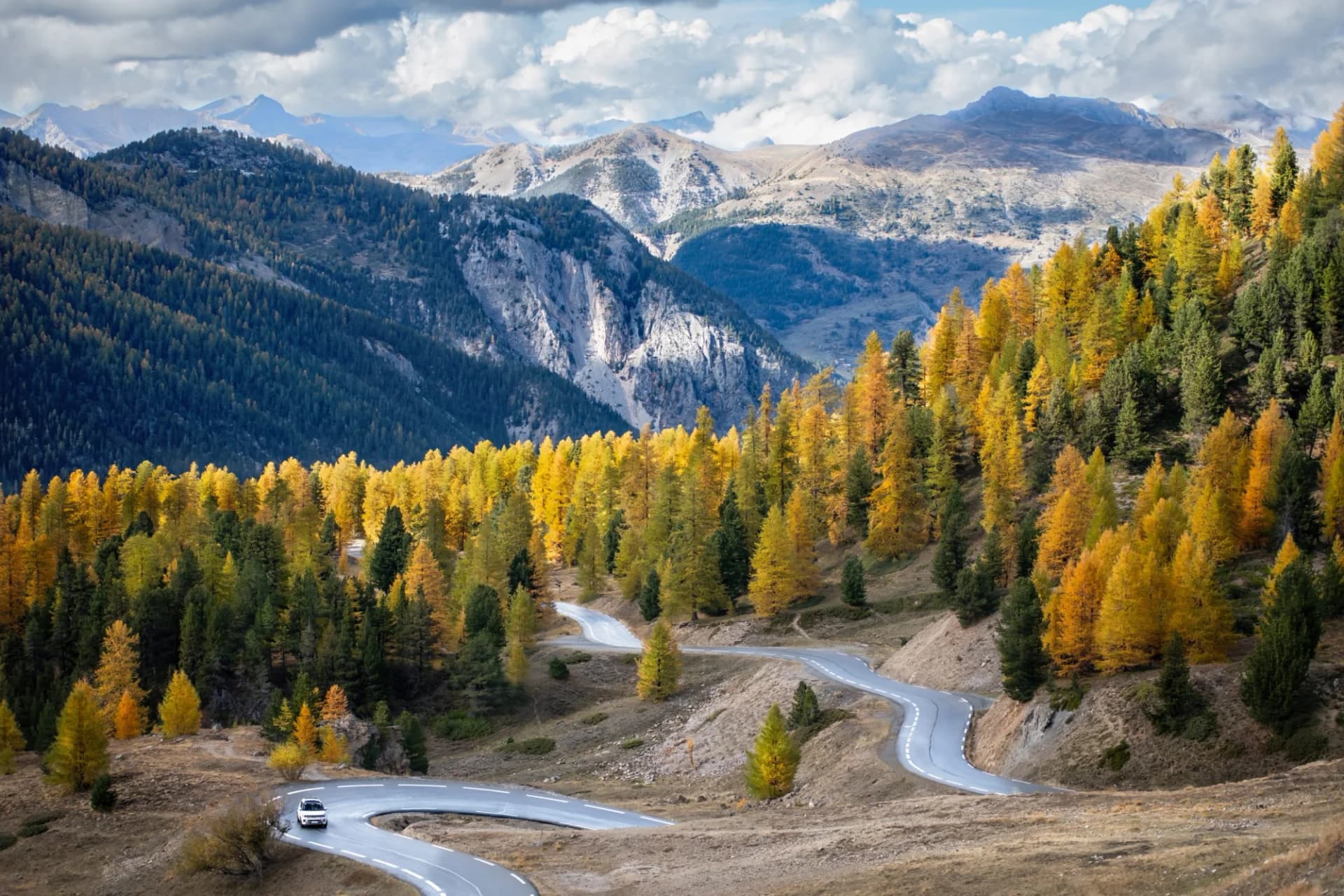Winding mountain road with autumn foliage and a car in the French Alps.