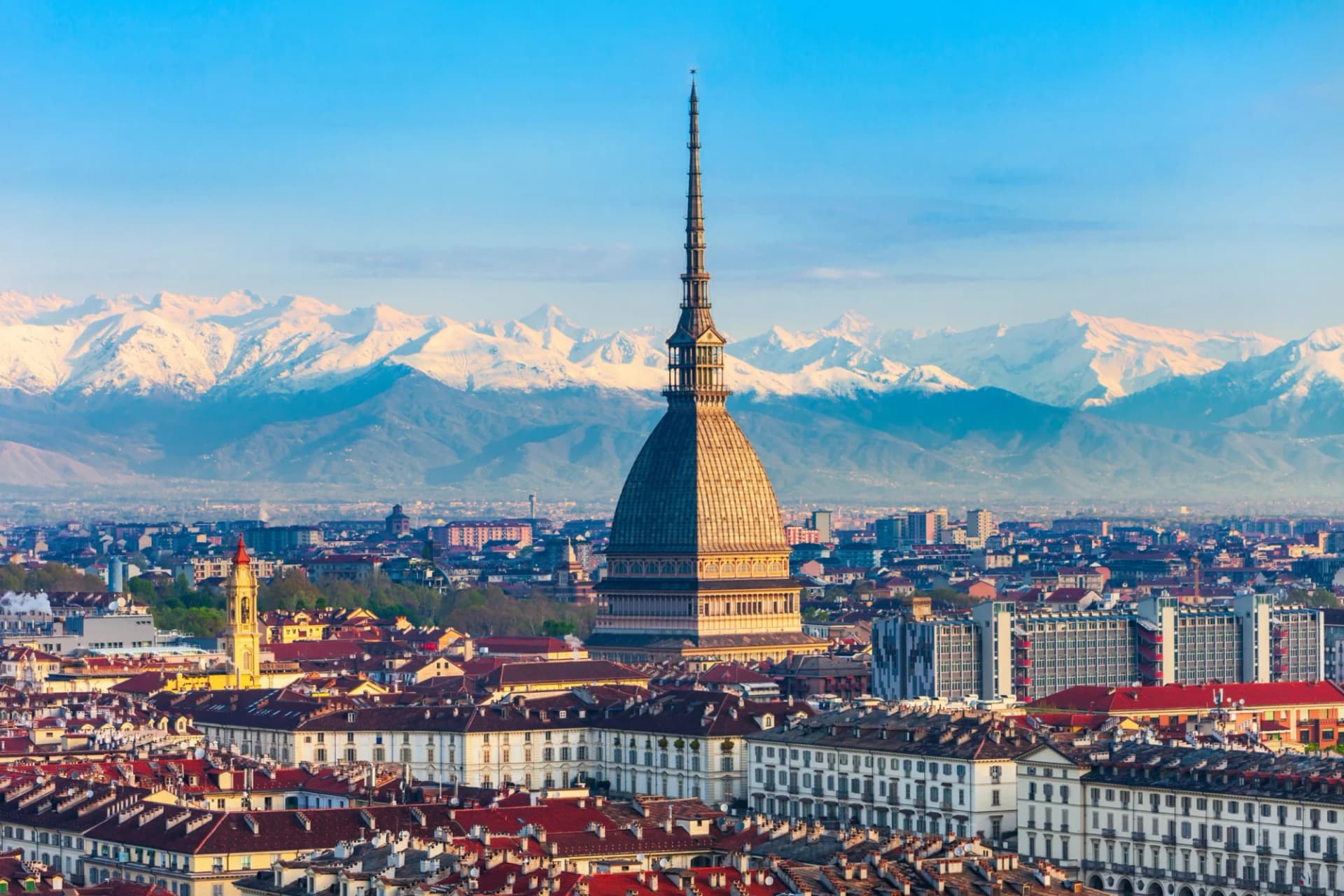 Aerial view of Mole Antonelliana in Turin skyline with snow-capped Alps in background.
