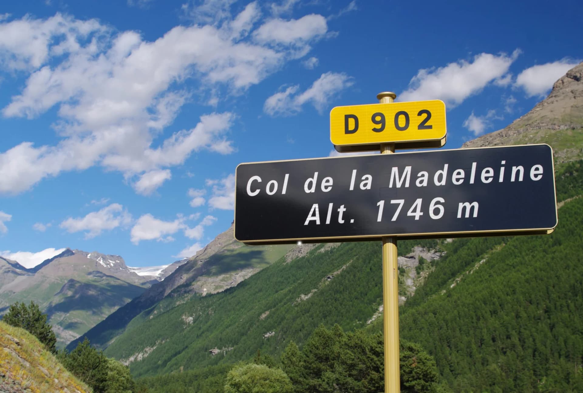 Col de la Madeleine D902 sign with altitude 1746m, set against green mountains and blue sky.
